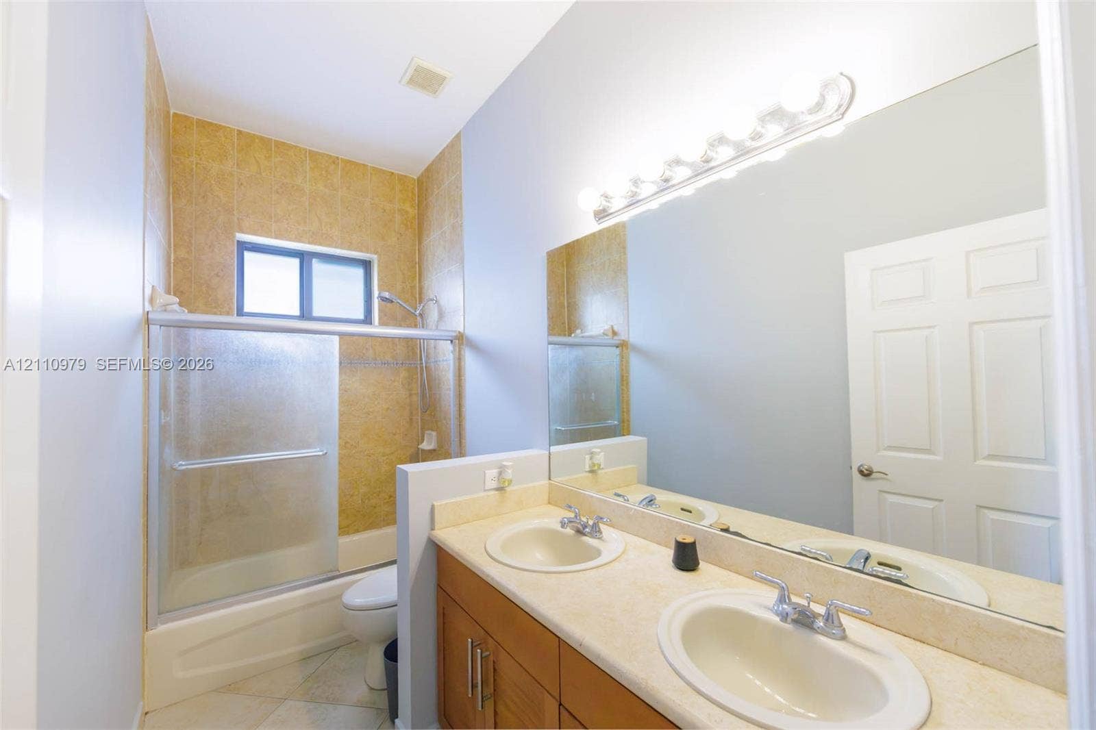 Bathroom featuring a dual-sink vanity with solid-surface countertops, wood-finish cabinetry, a full-width wall mirror, and a tub-shower combination with tiled surround