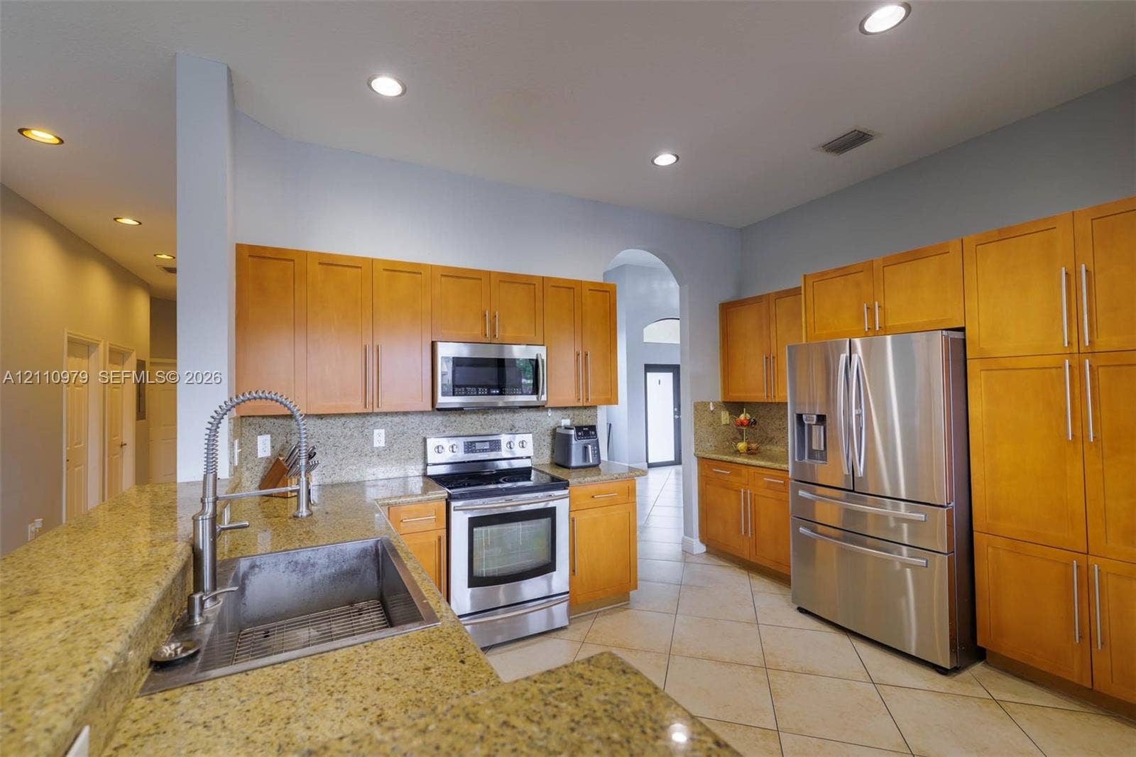 Kitchen featuring natural-finish wood cabinetry, stone countertops, stainless steel appliances, a deep undermount sink with a gooseneck faucet, and tile flooring