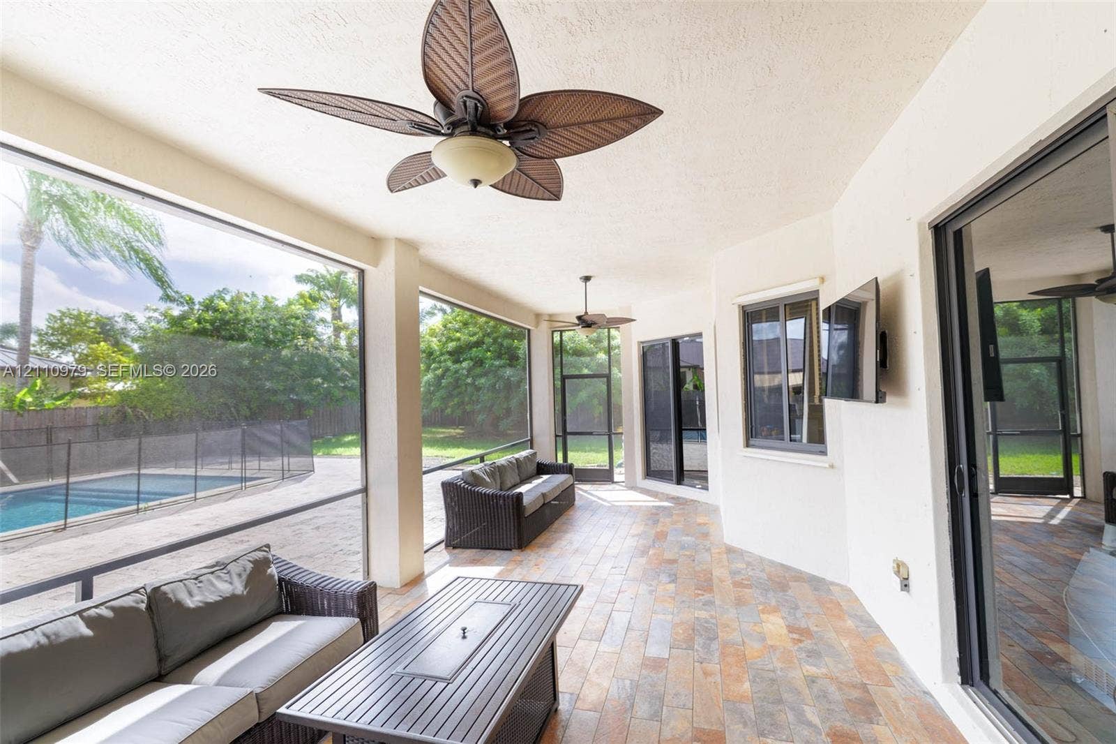 Screened-in lanai featuring tile flooring, ceiling fans, and an integrated pool area with security fencing