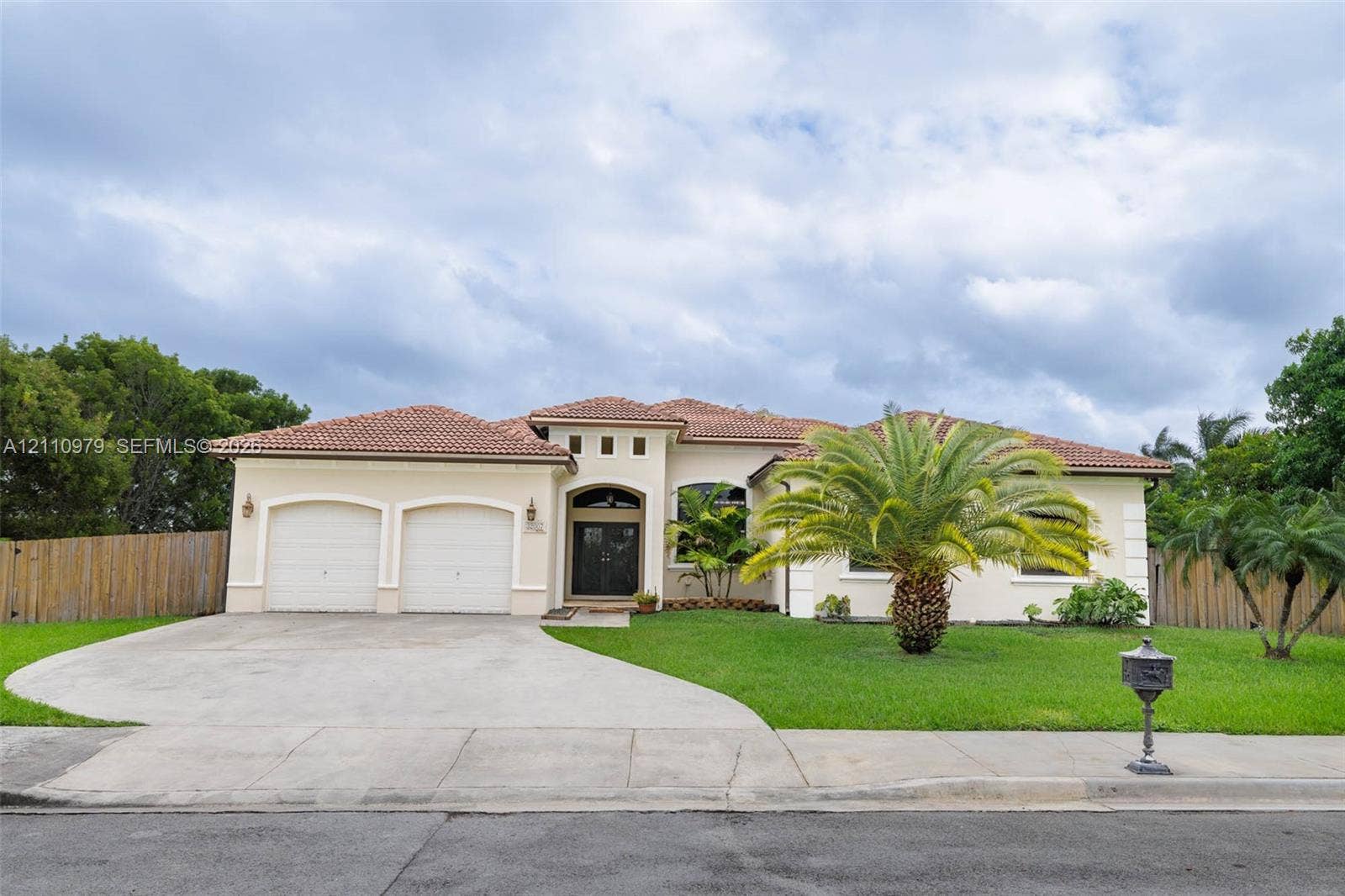 Single-story residence featuring a terracotta tile roof, stucco exterior, two-car garage, and an arched entry with a decorative front door