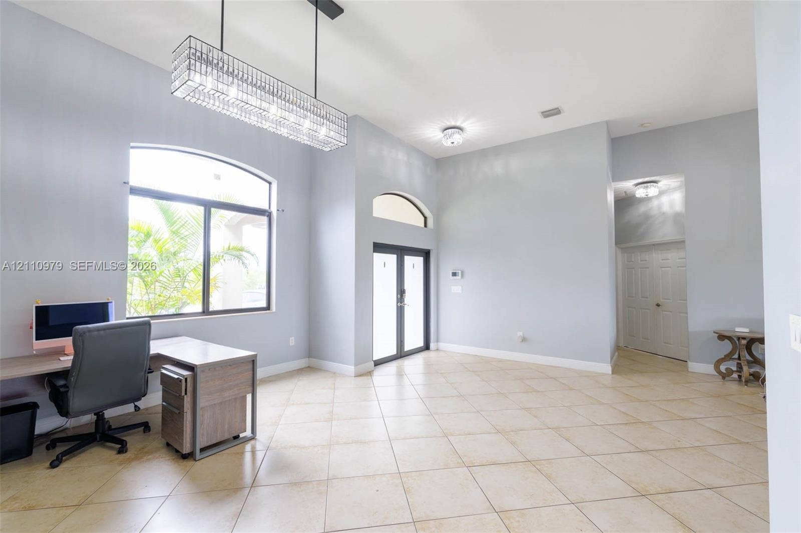 Open floor plan featuring high ceilings, large-format tile flooring, a geometric linear pendant light, an arched transom window, and double entry doors