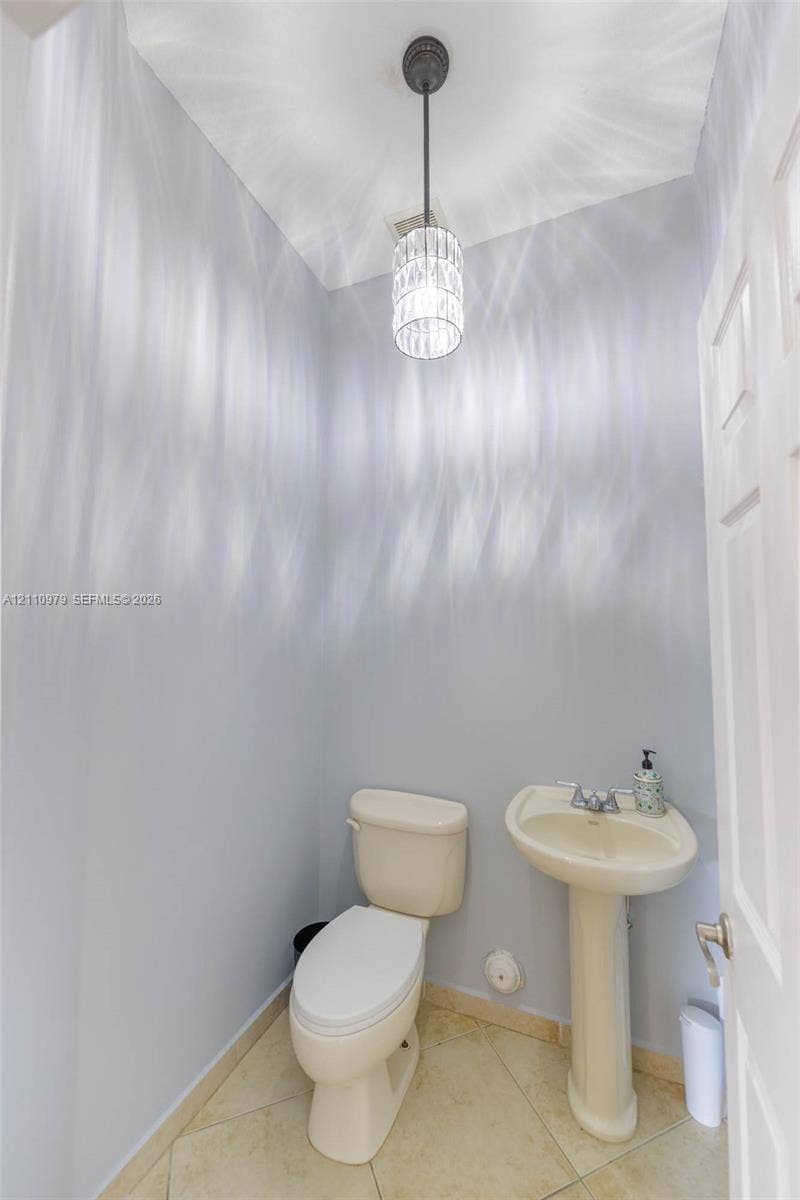 Neutral-toned powder room featuring a pedestal sink, dual-handle faucet, ceramic tile flooring, and a decorative cylinder pendant light fixture
