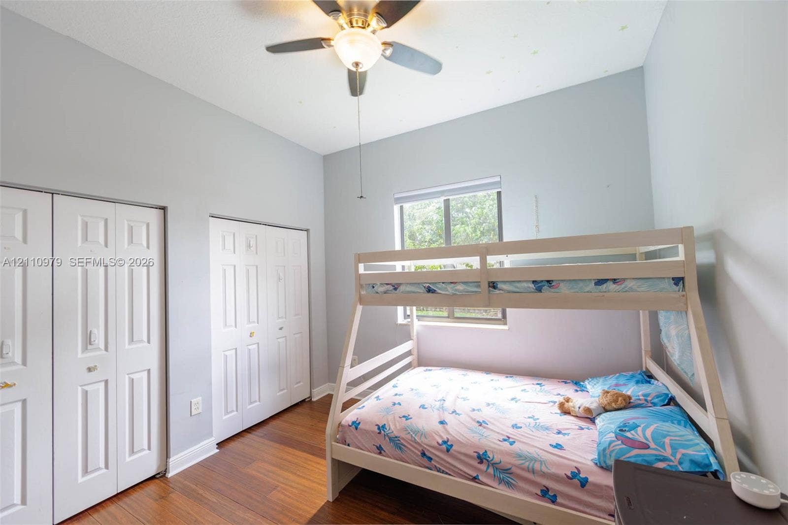 Room featuring wood-finish flooring, dual bi-fold door closets, recessed window, and a central ceiling fan with an integrated light fixture