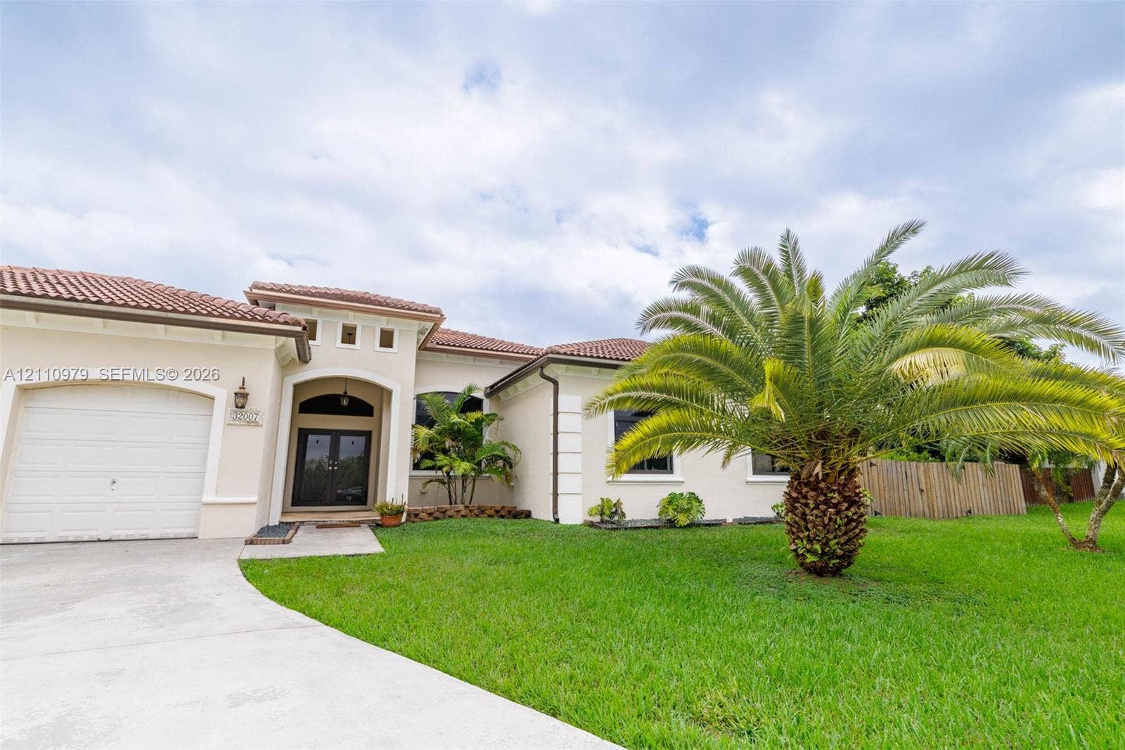 Stucco exterior with a tiled roof, arched entryway, double-door entrance, and an attached garage