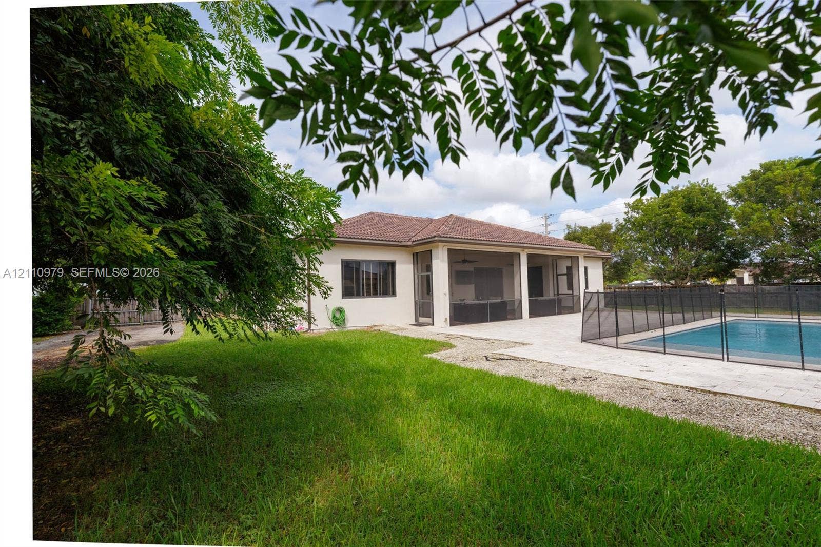 Backyard featuring a manicured lawn, a screen-enclosed covered patio, and a concrete pool deck surrounding an in-ground swimming pool with a removable safety fence
