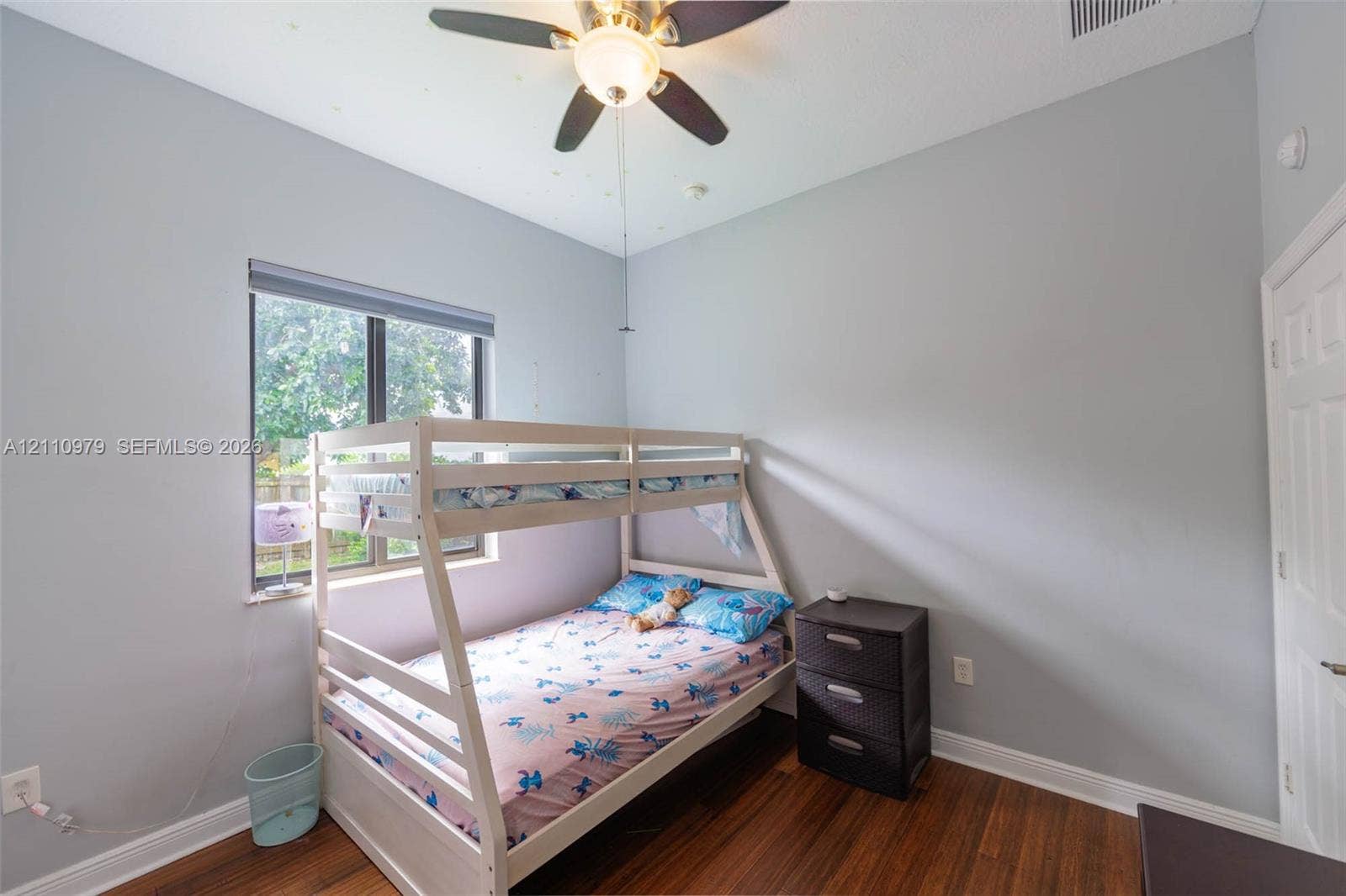 Room featuring wood-finish flooring, a ceiling fan with integrated lighting, and a single-panel window with a roller shade