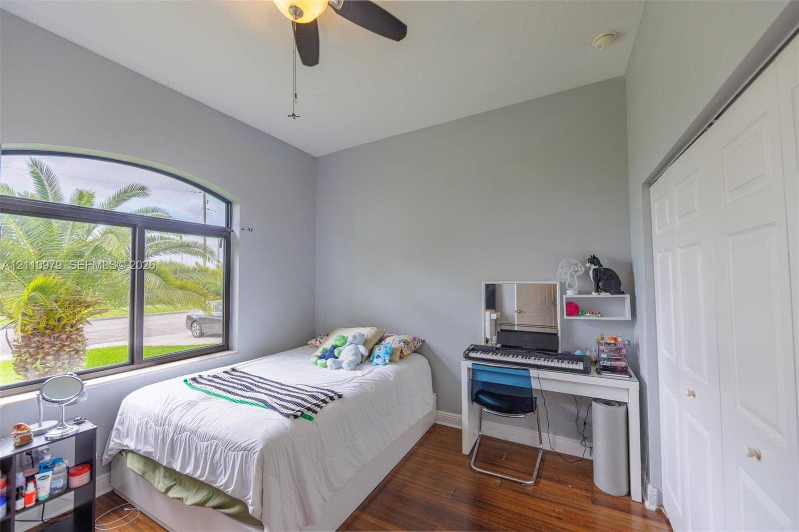 Room featuring arched window, dark wood-finish flooring, ceiling fan, and double-door closet