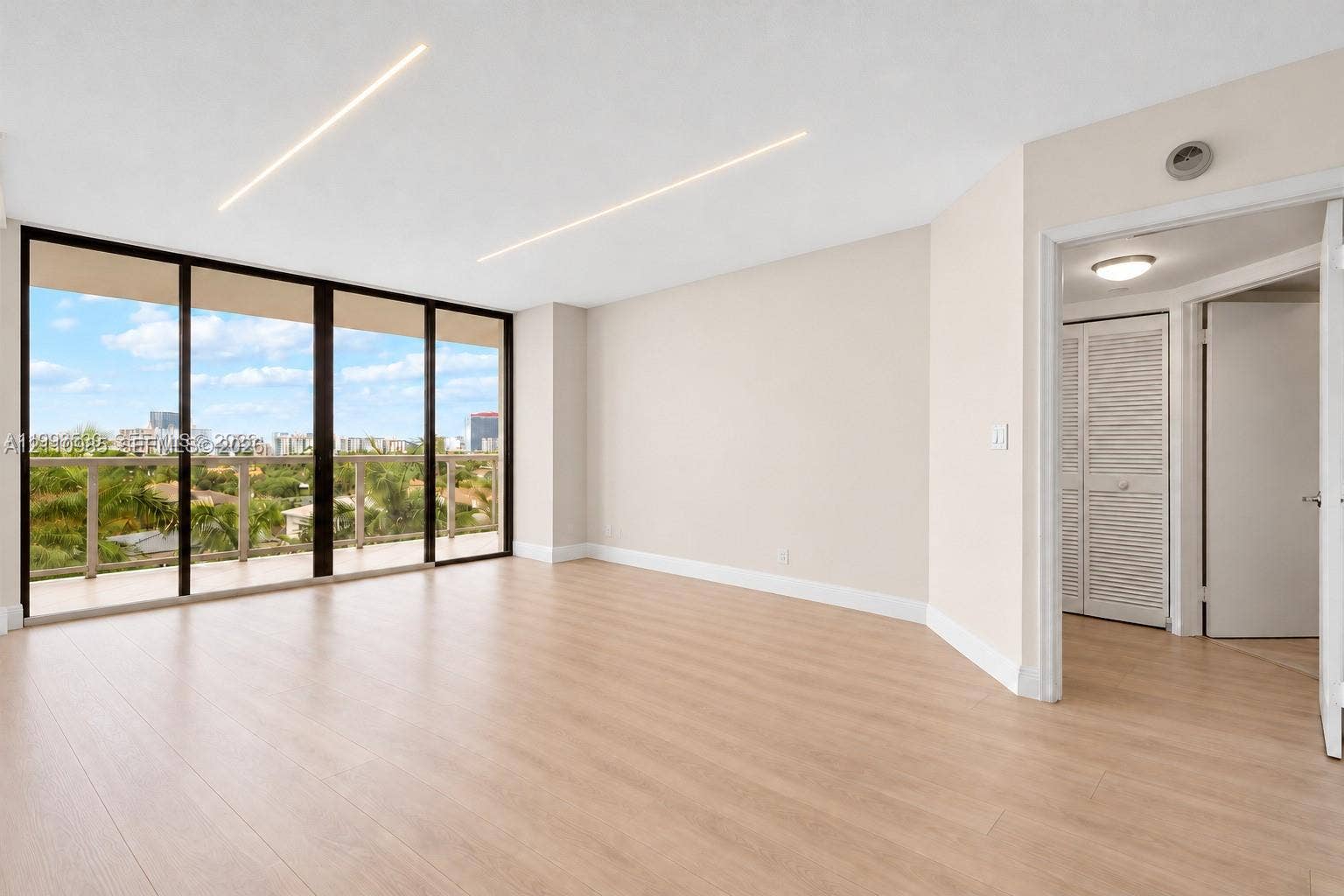 Virtually edited photo (digitally emptied/staged). Open-concept living space featuring floor-to-ceiling glass panel doors, wood-finish flooring, recessed linear lighting, and a closet with louvered doors.