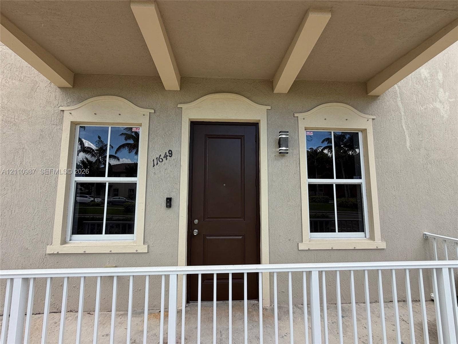 Covered entryway featuring a solid-panel door, decorative window pediments, and a white metal railing