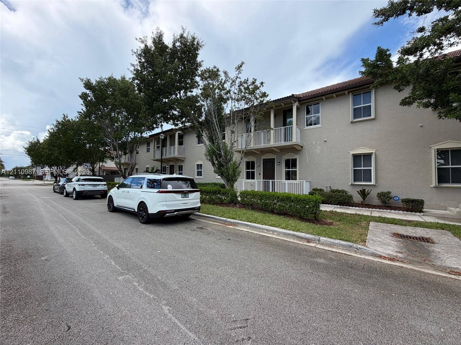 Two-story stucco exterior featuring covered balconies, recessed entryways, tile roof, and manicured shrubbery