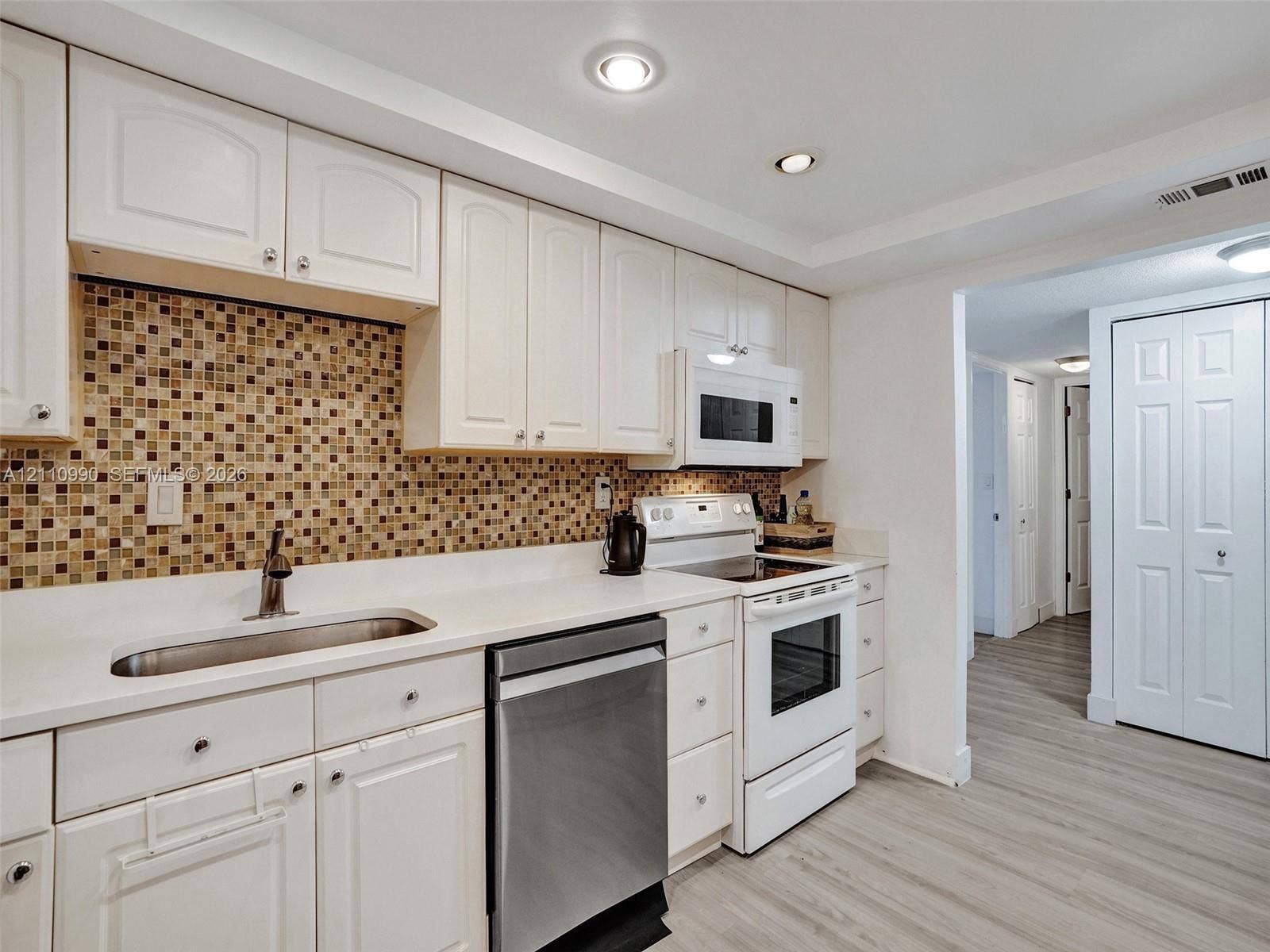 800 Parkview Drive, #131, Hallandale Beach, FL 33009 Kitchen featuring white cabinetry, solid-surface countertops, mosaic tile backsplash, stainless steel dishwasher, and wood-finish flooring