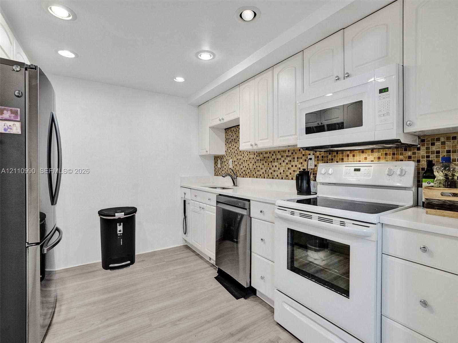 800 Parkview Drive, #131, Hallandale Beach, FL 33009 Kitchen featuring white cabinetry, mosaic tile backsplash, solid surface countertops, wood-finish flooring, and stainless steel appliances