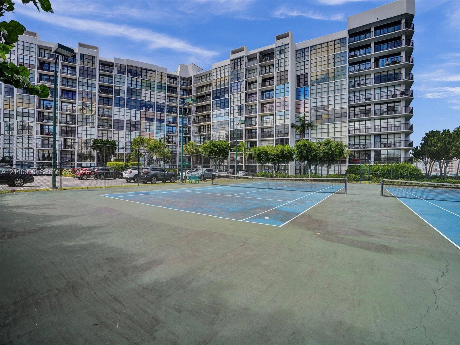 800 Parkview Drive, #131, Hallandale Beach, FL 33009 Hard-surfaced tennis court featuring chain-link fencing and net system, situated on the premises of a multi-story residential building with glass-paneled balconies