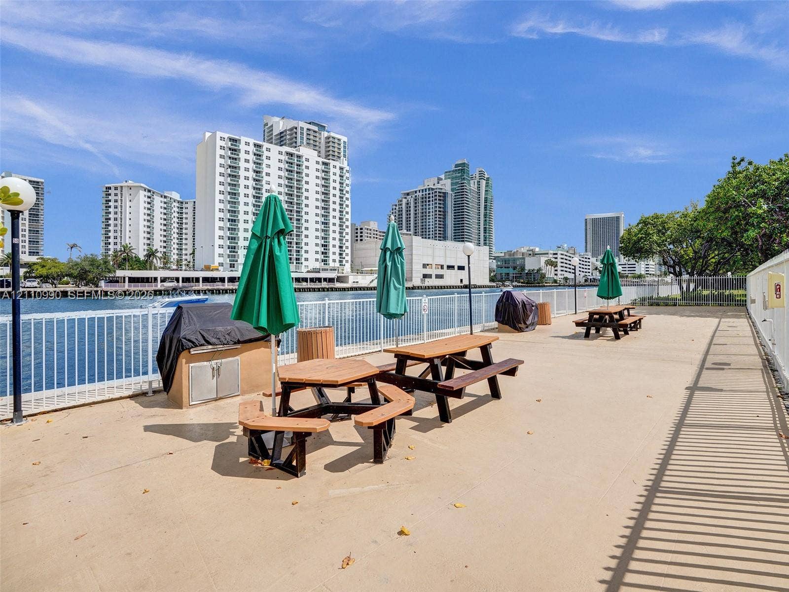 800 Parkview Drive, #131, Hallandale Beach, FL 33009 Waterfront terrace featuring a concrete deck, metal perimeter fencing, built-in stainless steel grilling station, and pole-mounted outdoor lighting