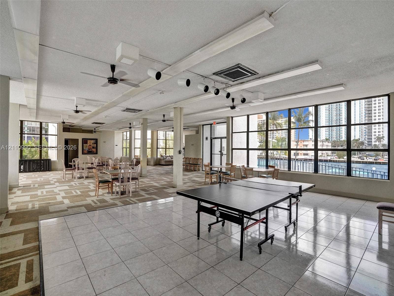 800 Parkview Drive, #131, Hallandale Beach, FL 33009 Open-concept interior featuring extensive floor-to-ceiling windows, ceramic tile flooring, patterned carpet, industrial-style track lighting, and ceiling fans