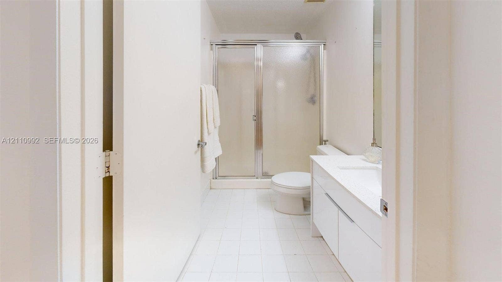 Bathroom featuring a white vanity cabinet, solid-surface countertop with an integrated sink, shower enclosure with a metallic frame, and ceramic tile flooring