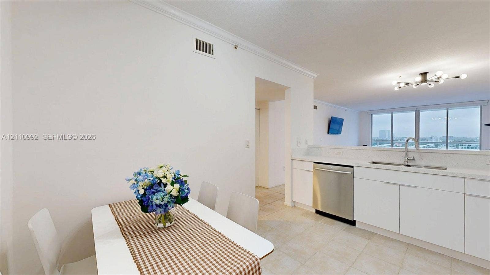 Kitchen featuring white cabinetry, stainless steel dishwasher, integrated sink, and tile flooring, illuminated by a multi-bulb modern ceiling fixture