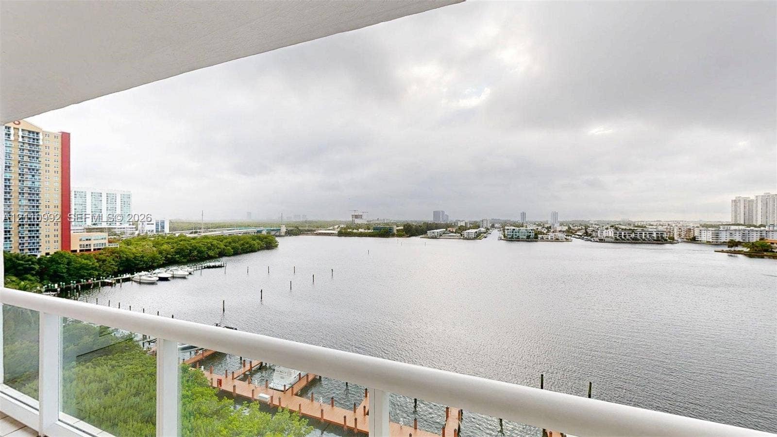 Balcony featuring a white railing with glass panels, overlooking a waterway with private boat docks