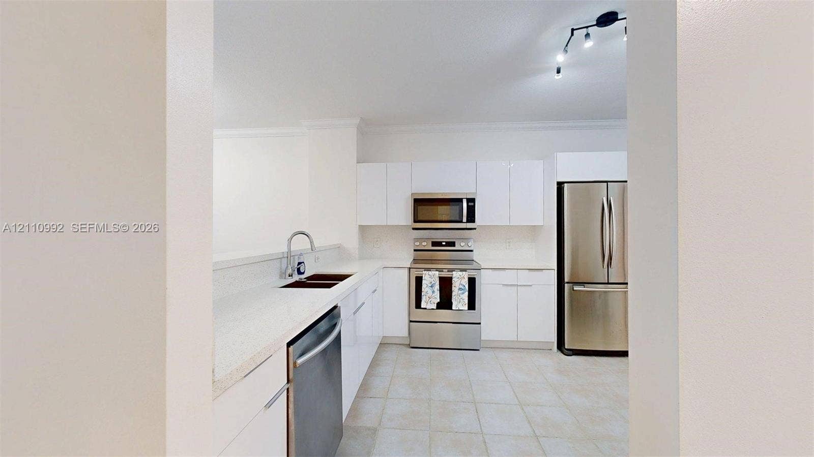 Kitchen featuring white slab cabinetry, stainless steel appliances, solid-surface countertops, dual-basin undermount sink, and tile flooring