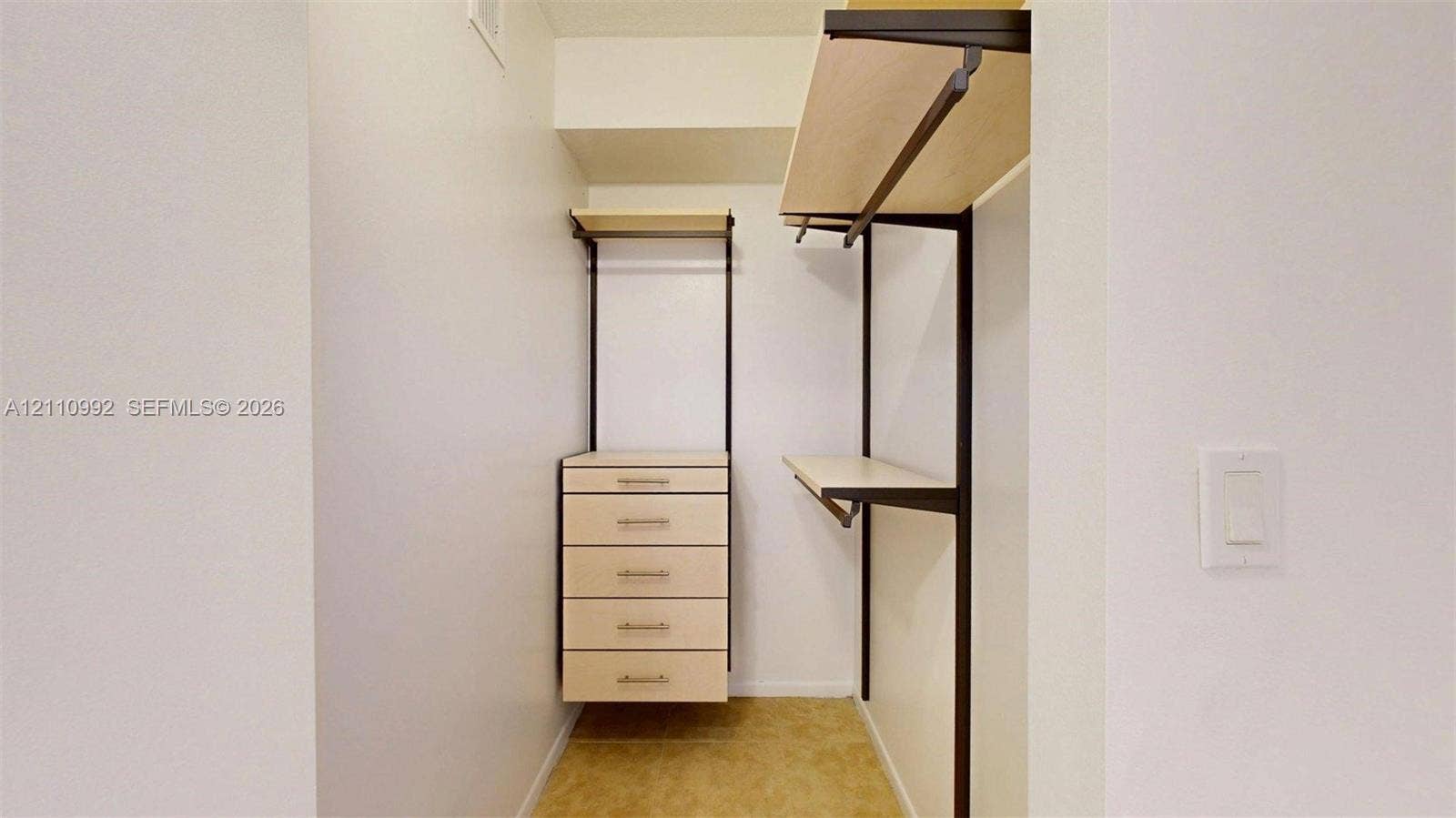 Walk-in closet featuring light-toned custom shelving, a built-in five-drawer chest, and dark metal hardware finishes