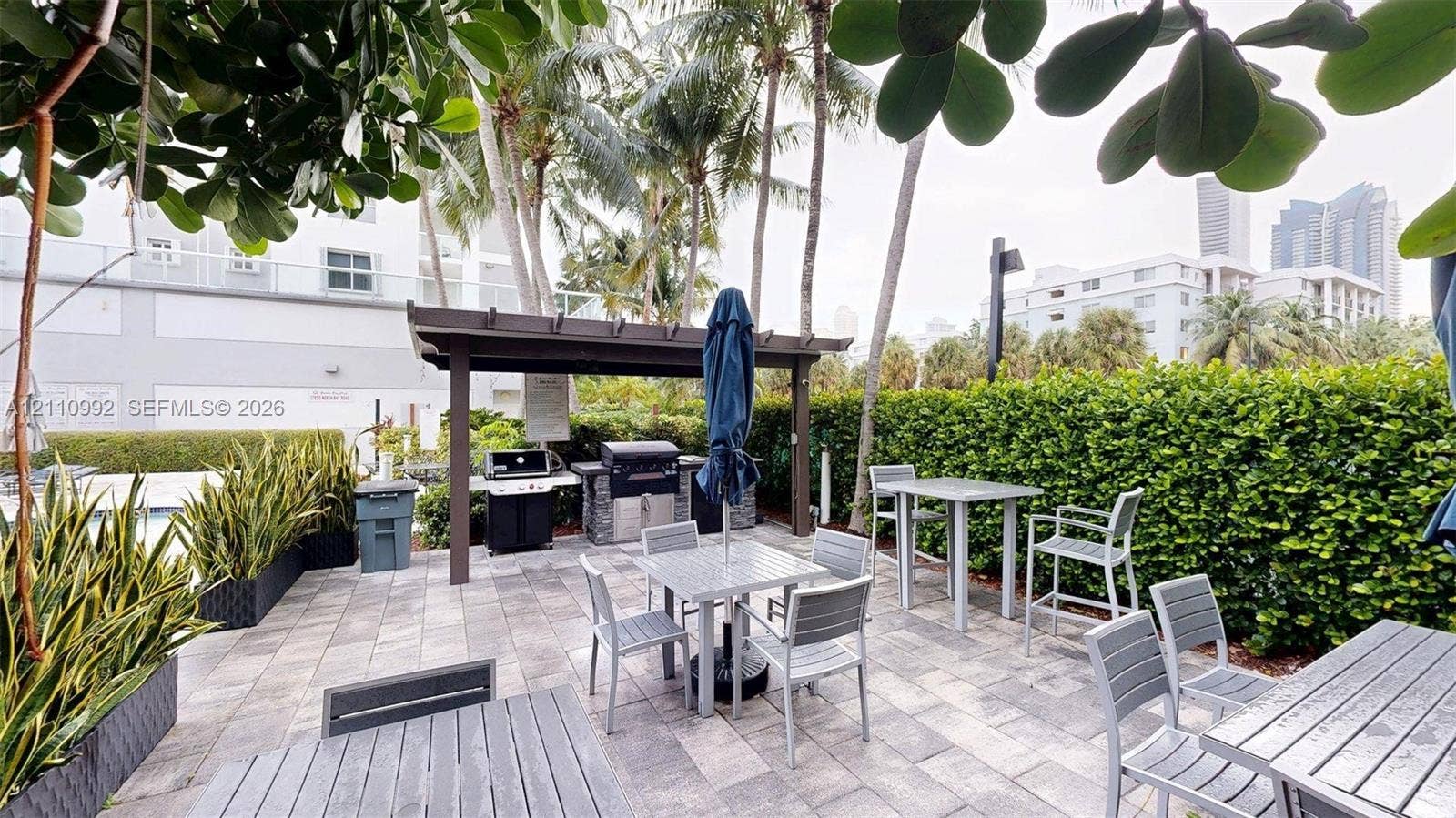 Outdoor patio featuring stone paver flooring, a wood-frame pergola, and a built-in outdoor kitchen with stone veneer detailing