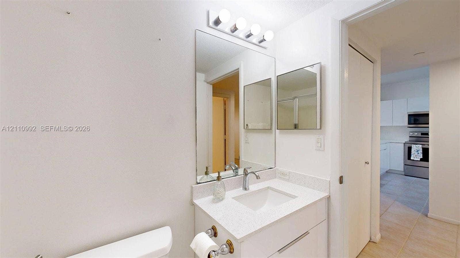 Bathroom vanity featuring a stone-composite countertop, undermount sink, chrome faucet, full-height wall mirror, and integrated lighting