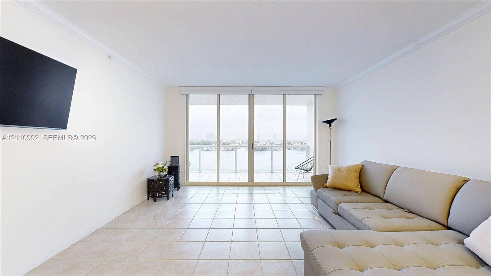 Living space featuring large-format tile flooring, crown molding, and sliding glass doors that open to a balcony with metal railings and water scenery