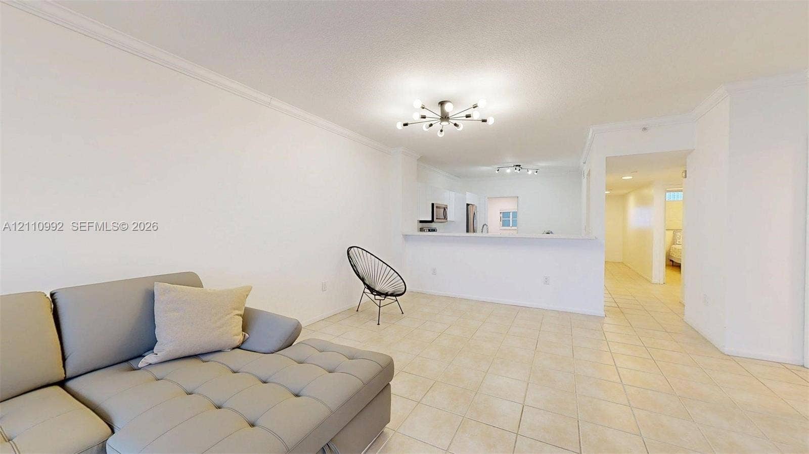 Neutral tile flooring, crown molding, multi-arm flush-mount lighting, and a breakfast bar counter