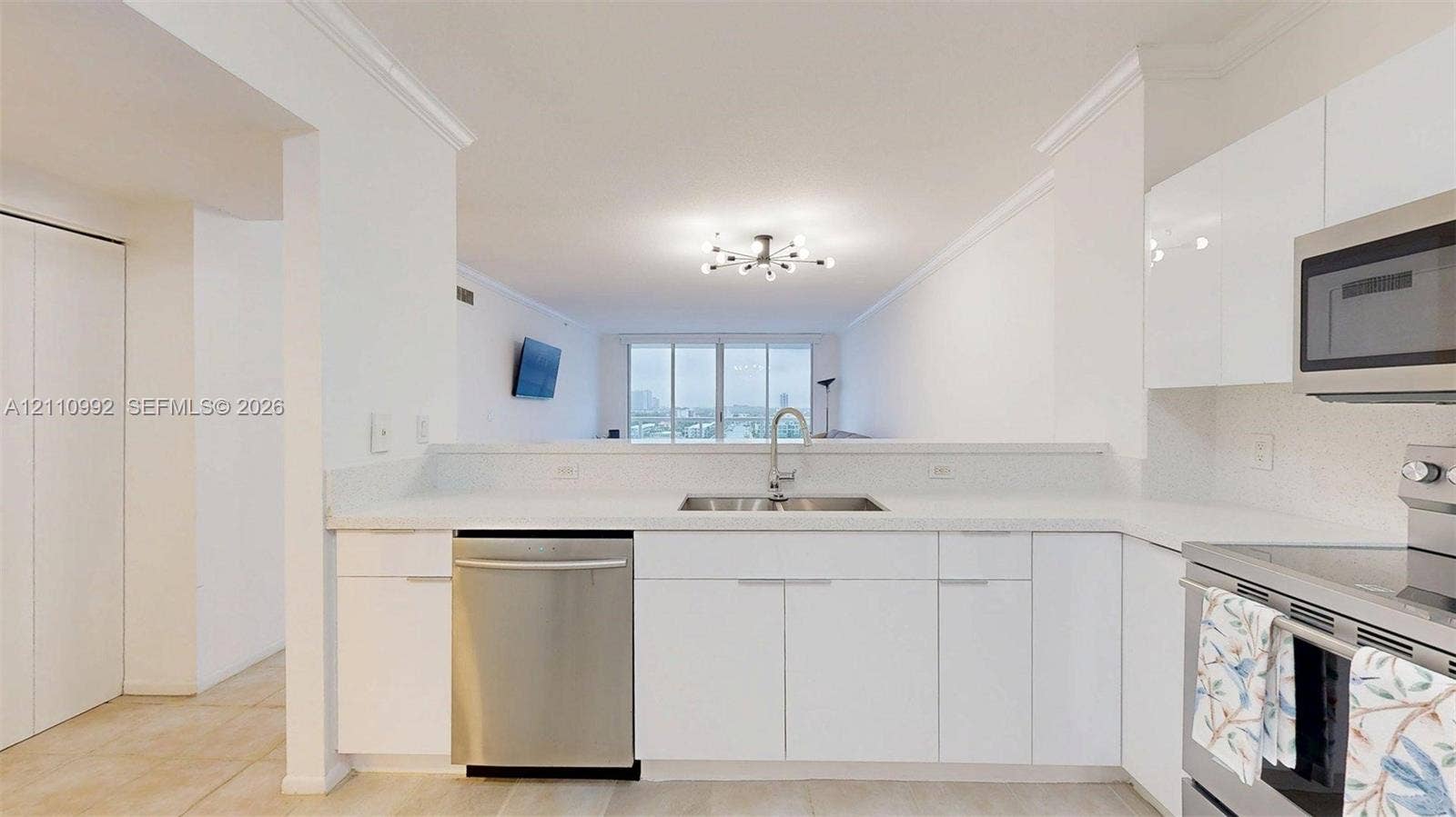 Kitchen featuring white flat-panel cabinetry, light-toned countertops, stainless steel appliances, and a polished chrome faucet with a dual-basin sink