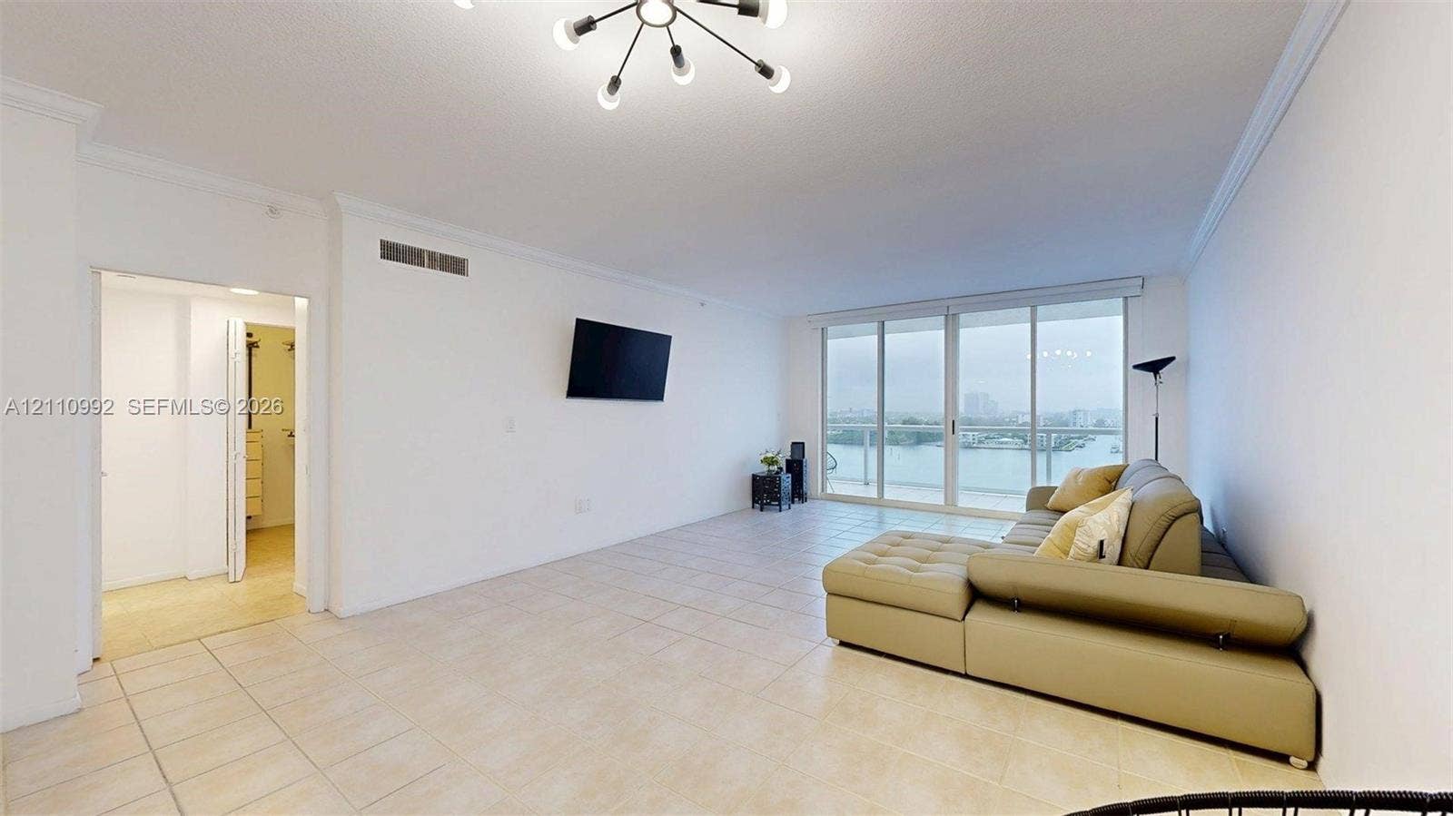 Open-concept living space featuring large-format tile flooring, a multi-arm modern ceiling light fixture, expansive floor-to-ceiling glass sliding doors, and a private balcony