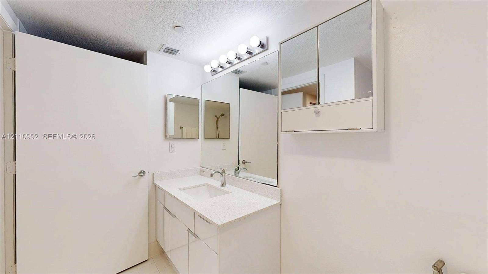 Bathroom vanity featuring a solid surface countertop, integrated rectangular sink, chrome fixtures, built-in medicine cabinet, and wall-mounted multi-bulb lighting