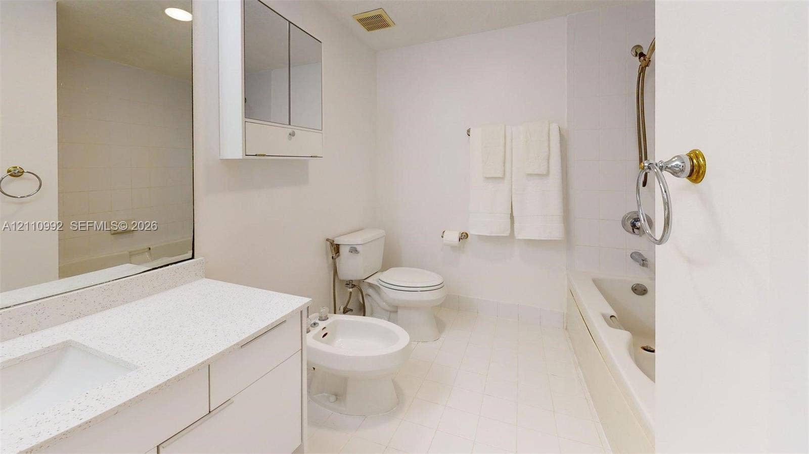 Bathroom featuring a vanity with a white countertop and integrated sink, a built-in medicine cabinet, a bidet, and a bathtub with a handheld shower fixture