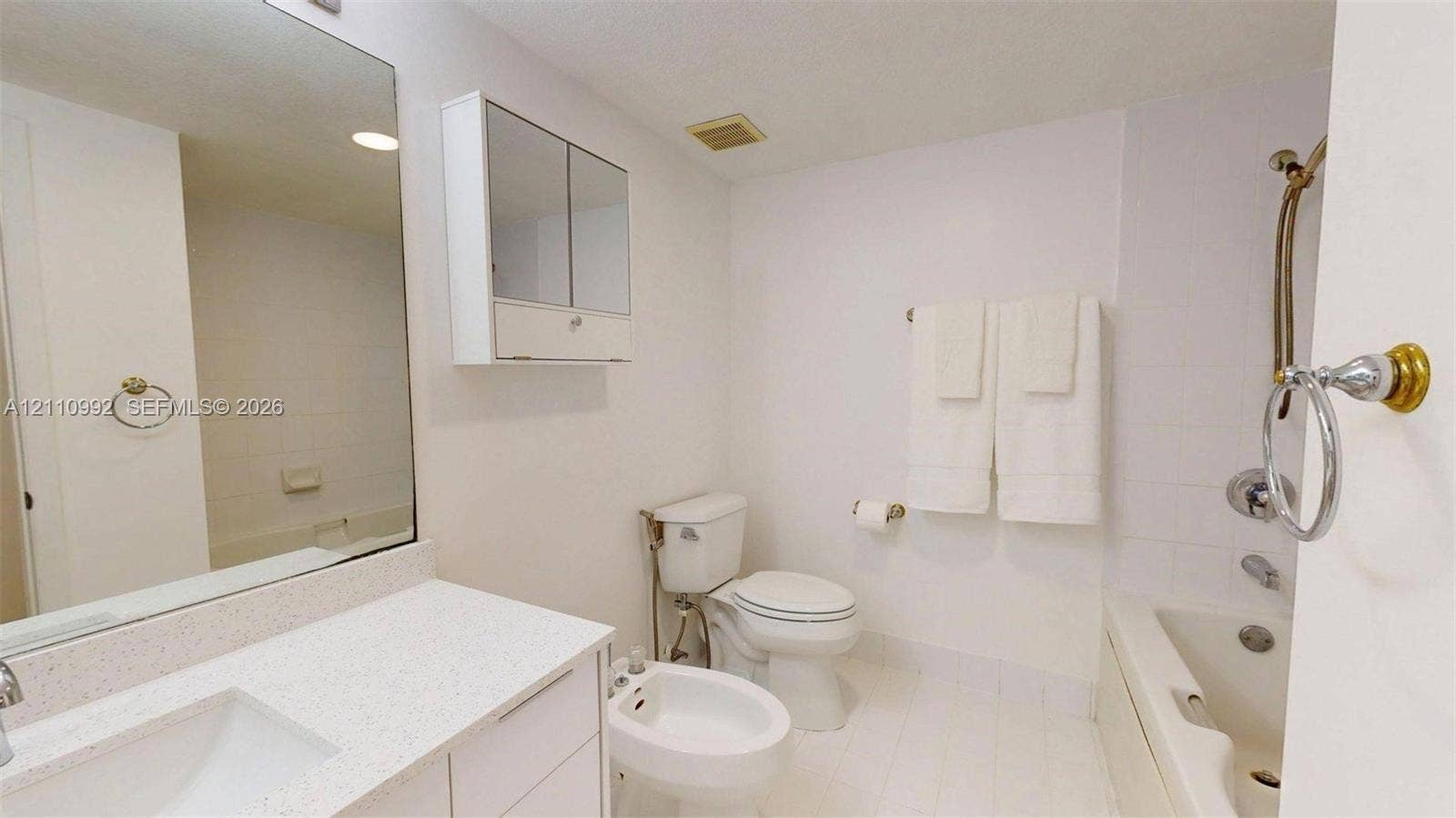 Bathroom featuring a stone-surface vanity countertop, an integrated rectangular sink, a mirrored medicine cabinet, a bidet, and a tile-surround shower and tub combination