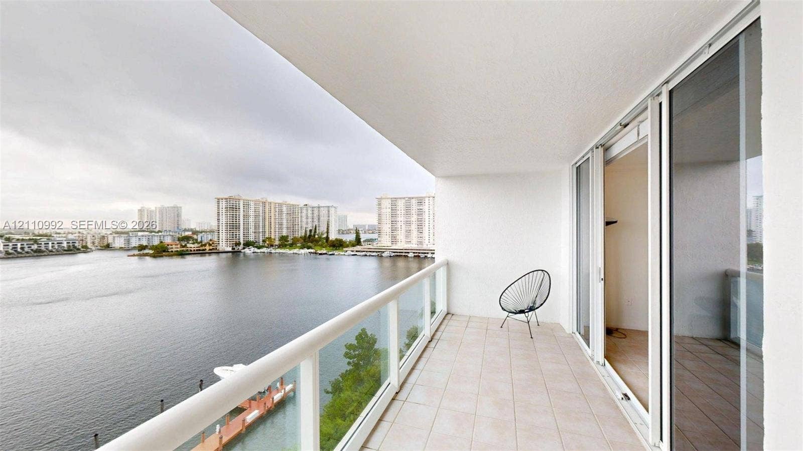 Private balcony featuring tile flooring and a glass-paneled railing, with sliding glass doors and expansive water frontage