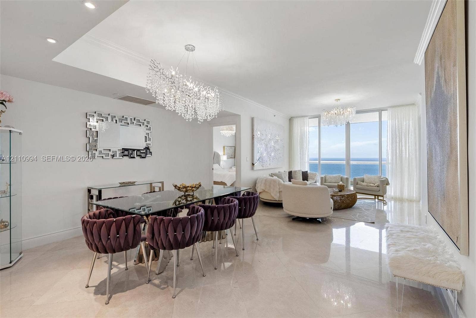 17875 Collins Avenue, #2405, Sunny Isles Beach, Sunny Isles Beach, FL 33160 Open-concept interior featuring light-toned polished stone flooring, recessed ceiling lighting, statement crystal chandeliers, and expansive floor-to-ceiling windows with ocean scenery