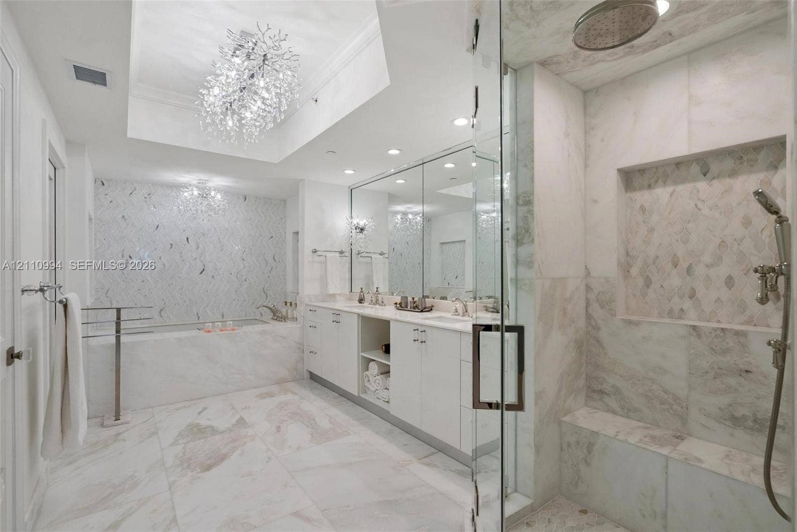 17875 Collins Avenue, #2405, Sunny Isles Beach, Sunny Isles Beach, FL 33160 Bathroom featuring a white double-vanity, walk-in glass-enclosed shower with a built-in bench, soaking tub with decorative tile surround, and crystal chandelier lighting
