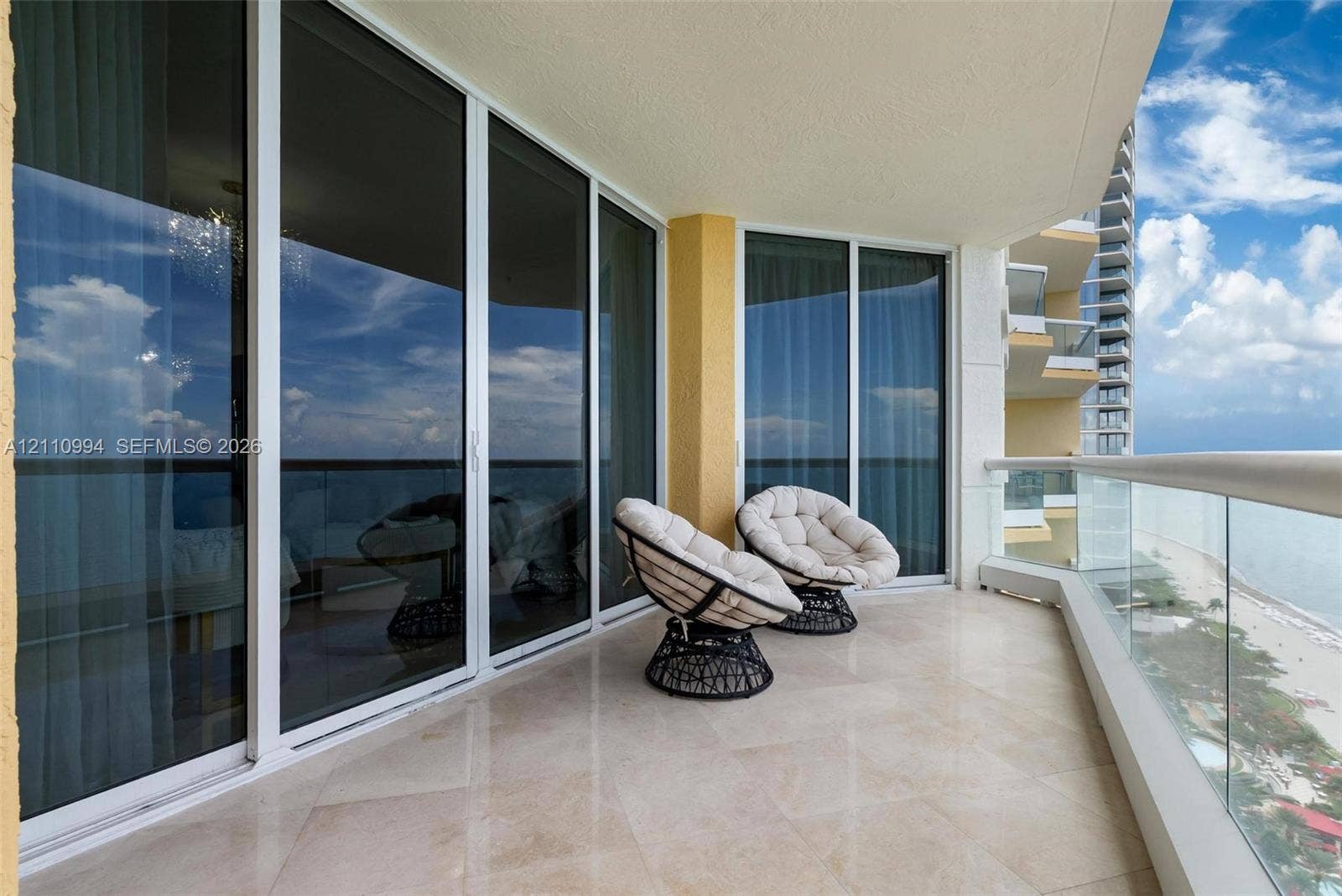 17875 Collins Avenue, #2405, Sunny Isles Beach, Sunny Isles Beach, FL 33160 Covered balcony featuring stone tile flooring, floor-to-ceiling glass sliding doors, and a transparent glass pane railing