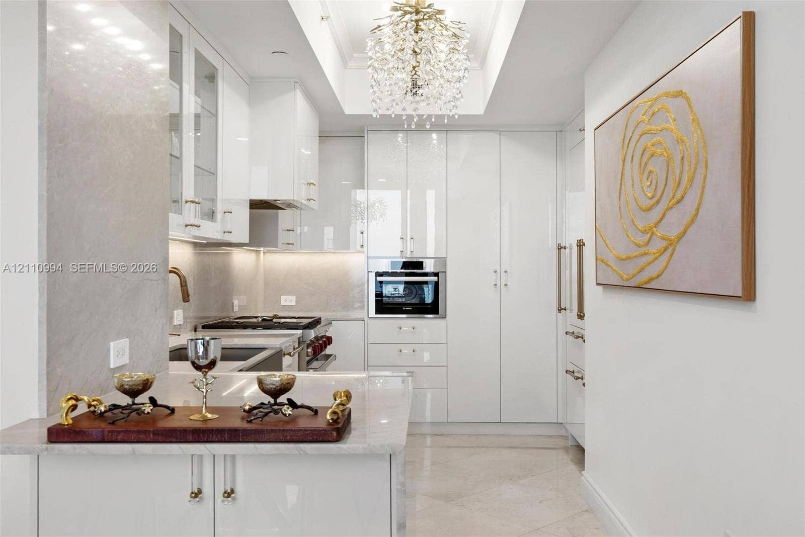 17875 Collins Avenue, #2405, Sunny Isles Beach, Sunny Isles Beach, FL 33160 High-gloss white cabinetry featuring polished hardware, stone-finish countertops, recessed tray ceiling with crystal-style chandelier, and built-in stainless steel wall oven