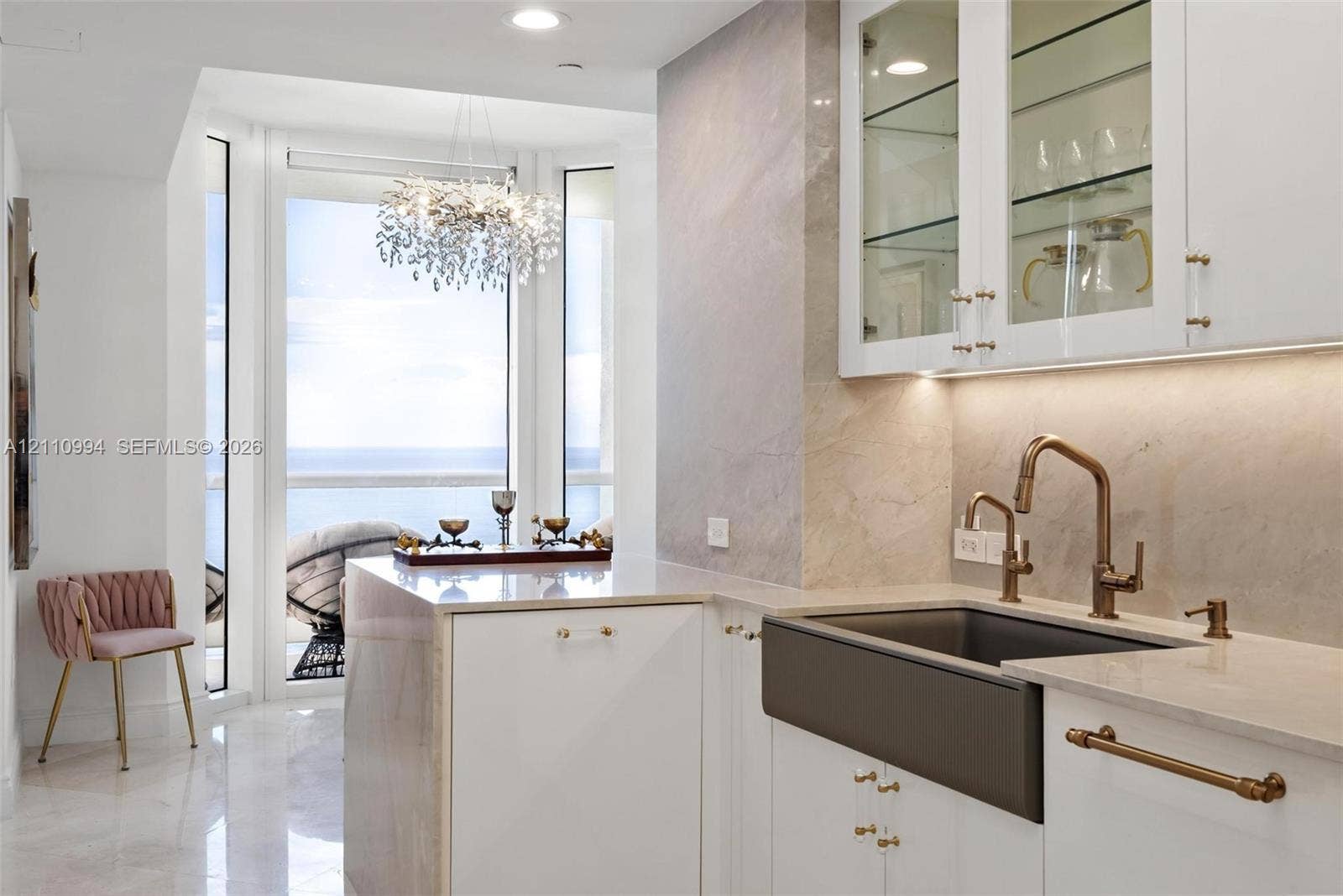 17875 Collins Avenue, #2405, Sunny Isles Beach, Sunny Isles Beach, FL 33160 Custom kitchen featuring white cabinetry with glass-front uppers, stone-surround backsplash, farmhouse sink with bronze-tone hardware, and light-reflecting flooring