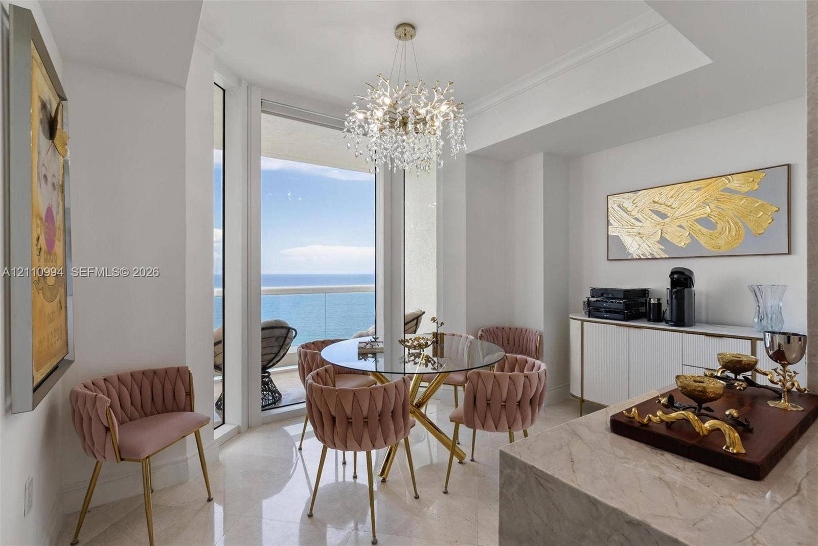 17875 Collins Avenue, #2405, Sunny Isles Beach, Sunny Isles Beach, FL 33160 Dining area featuring large-format polished stone flooring, floor-to-ceiling windows with ocean horizon, a multi-tiered crystal chandelier, and built-in white cabinetry with gold-tone hardware