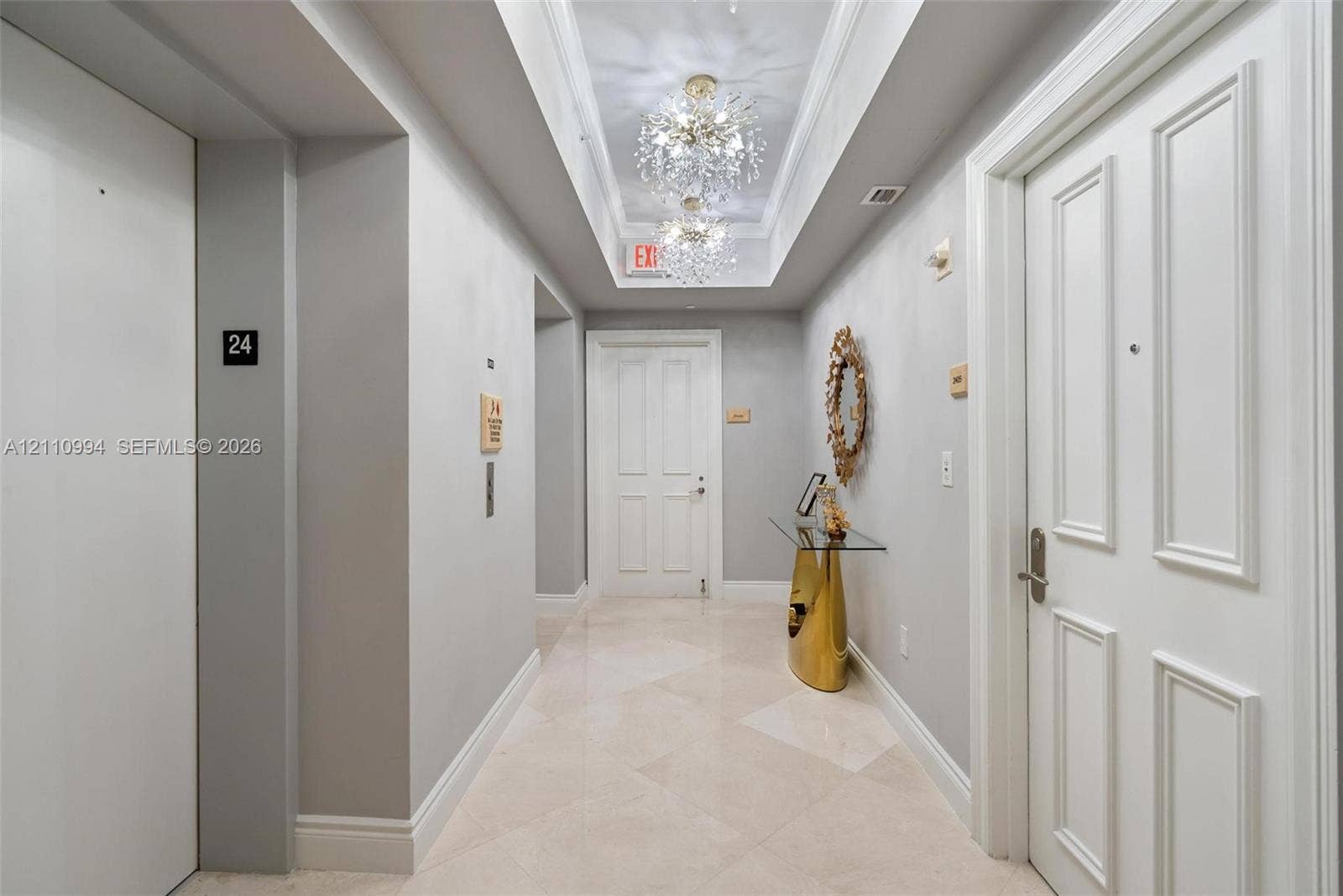 17875 Collins Avenue, #2405, Sunny Isles Beach, Sunny Isles Beach, FL 33160 Hallway featuring stone tile flooring, crown molding, dual crystal chandelier light fixtures set within a tray ceiling, and panel-style entry doors