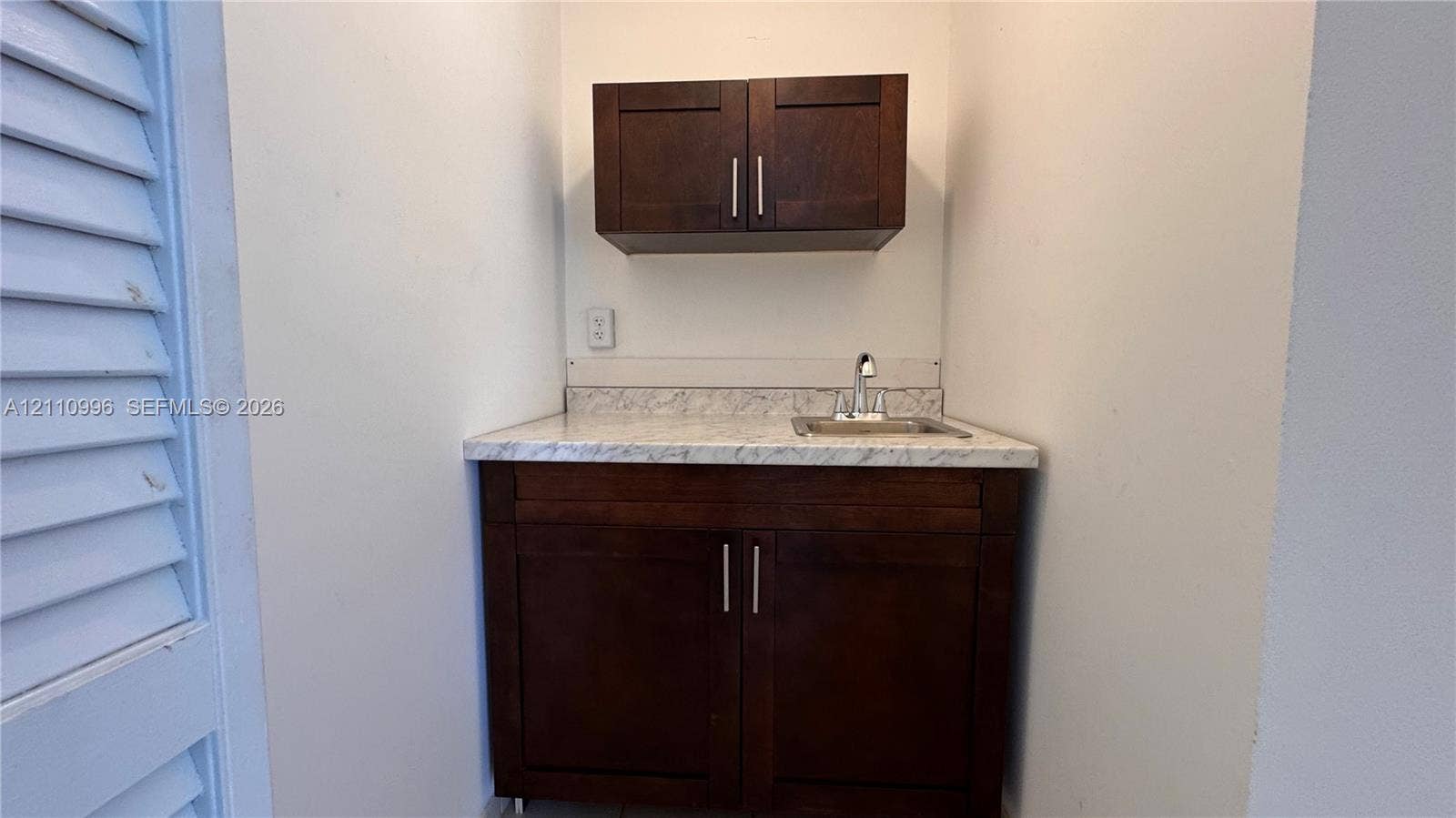 Built-in cabinetry featuring dark wood-finish doors, stone-patterned countertop, integrated basin, and metal faucet hardware