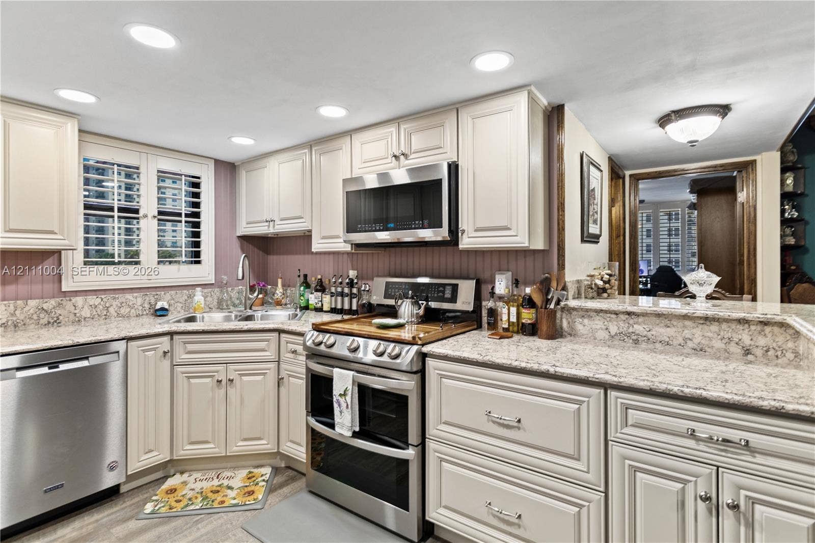 Kitchen featuring light-toned cabinetry, stone-finish countertops, stainless steel appliances, recessed lighting, and built-in shutter-style window coverings