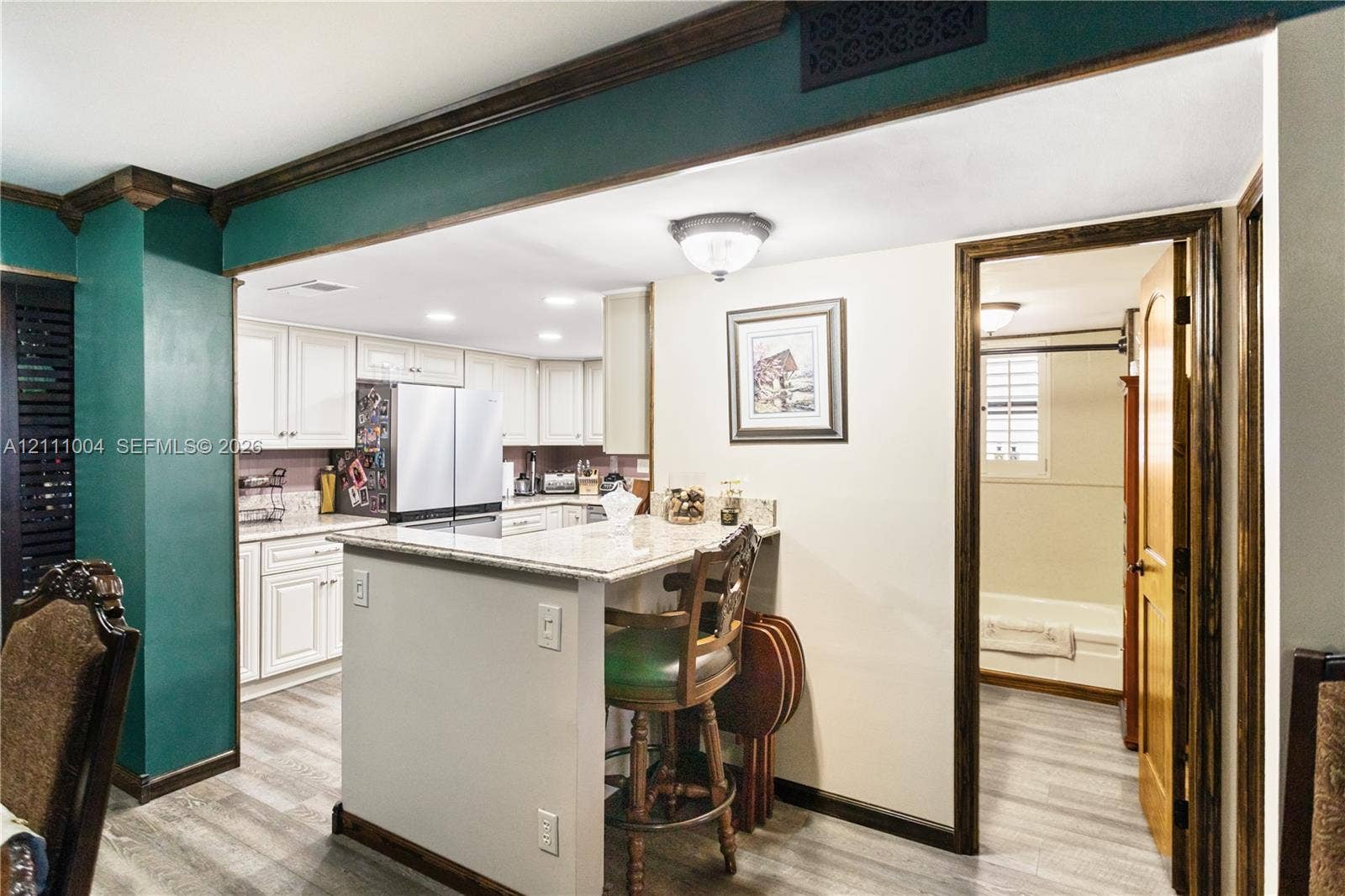 Kitchen featuring white shaker-style cabinetry, stone-surface countertops, a breakfast bar, and wood-finish flooring