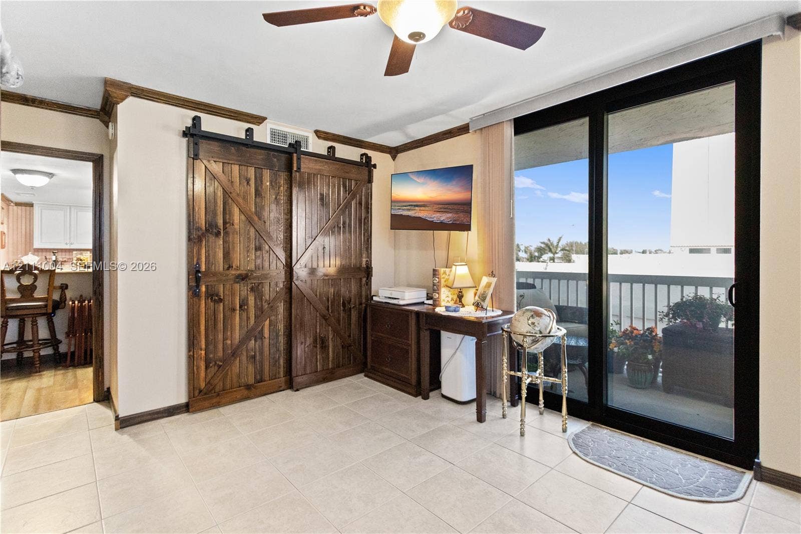 Interior room featuring tile flooring, sliding wood-finish barn doors, ceiling fan with light fixture, and floor-to-ceiling sliding glass doors