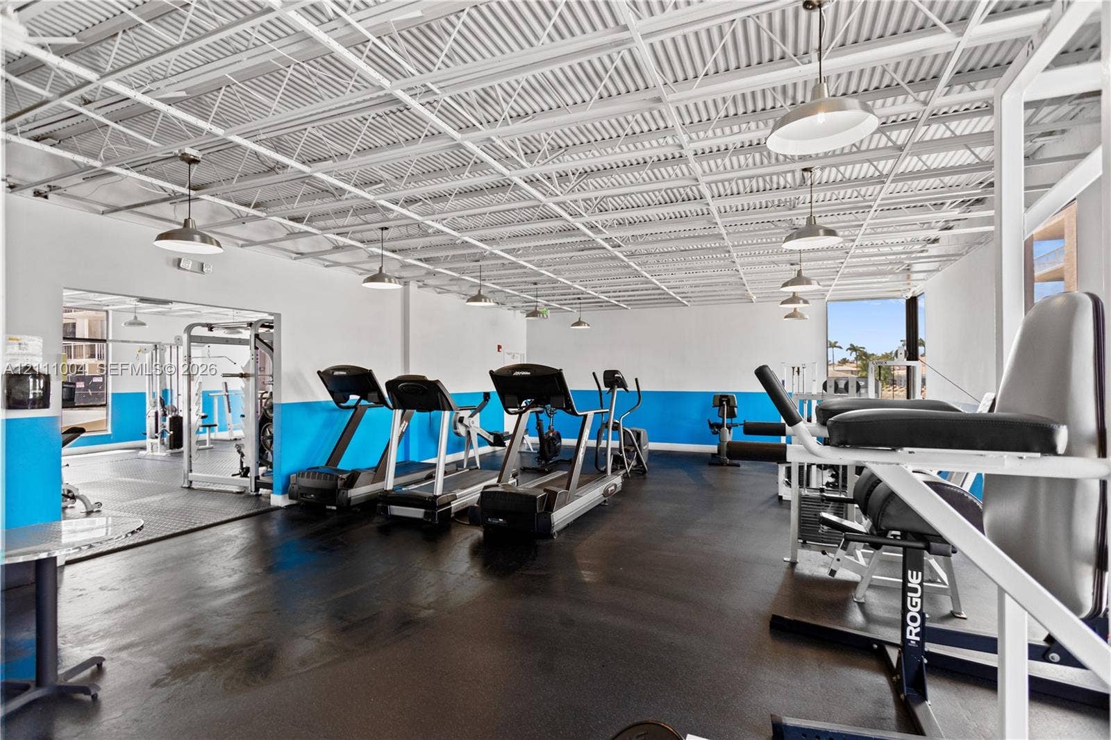 Fitness facility featuring an exposed corrugated metal ceiling, rubberized flooring, pendant lighting, and crisp white and blue wall finishes