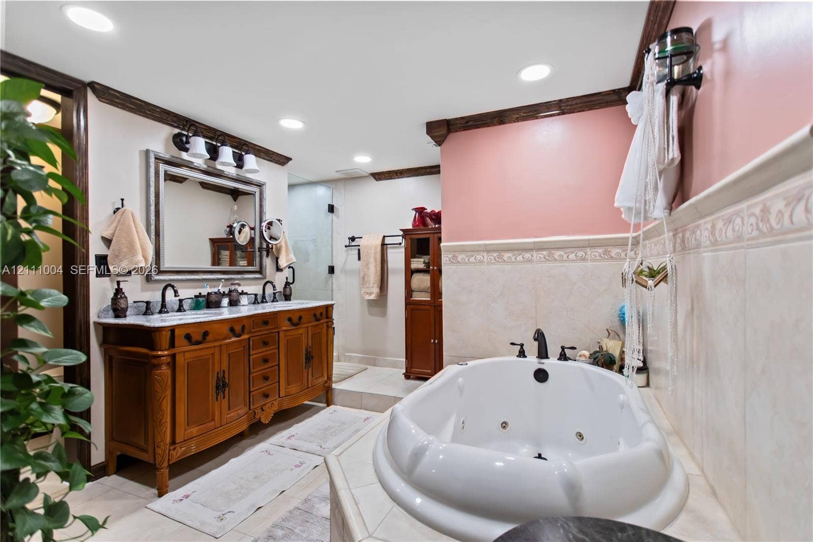 Bathroom featuring a custom wood vanity with a dual-sink stone countertop, a jetted soaking tub, tiled wainscoting, and recessed lighting