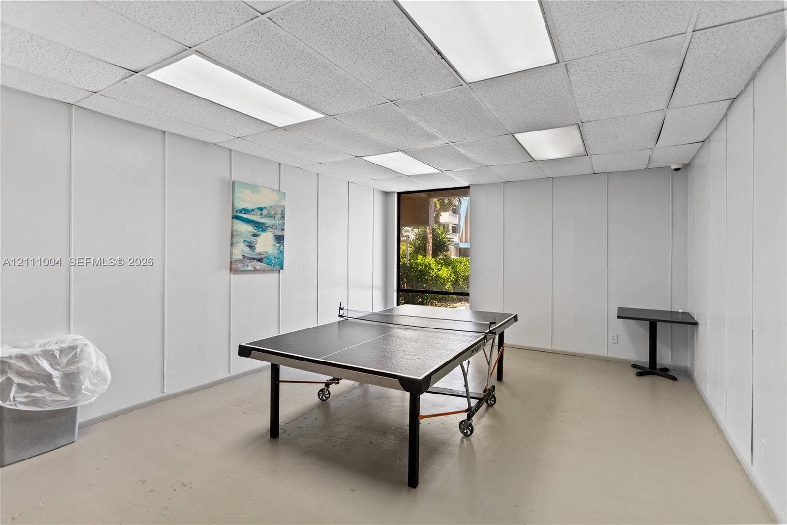 Interior room featuring white paneled walls, a drop ceiling with recessed lighting, smooth flooring, and a window with exterior greenery