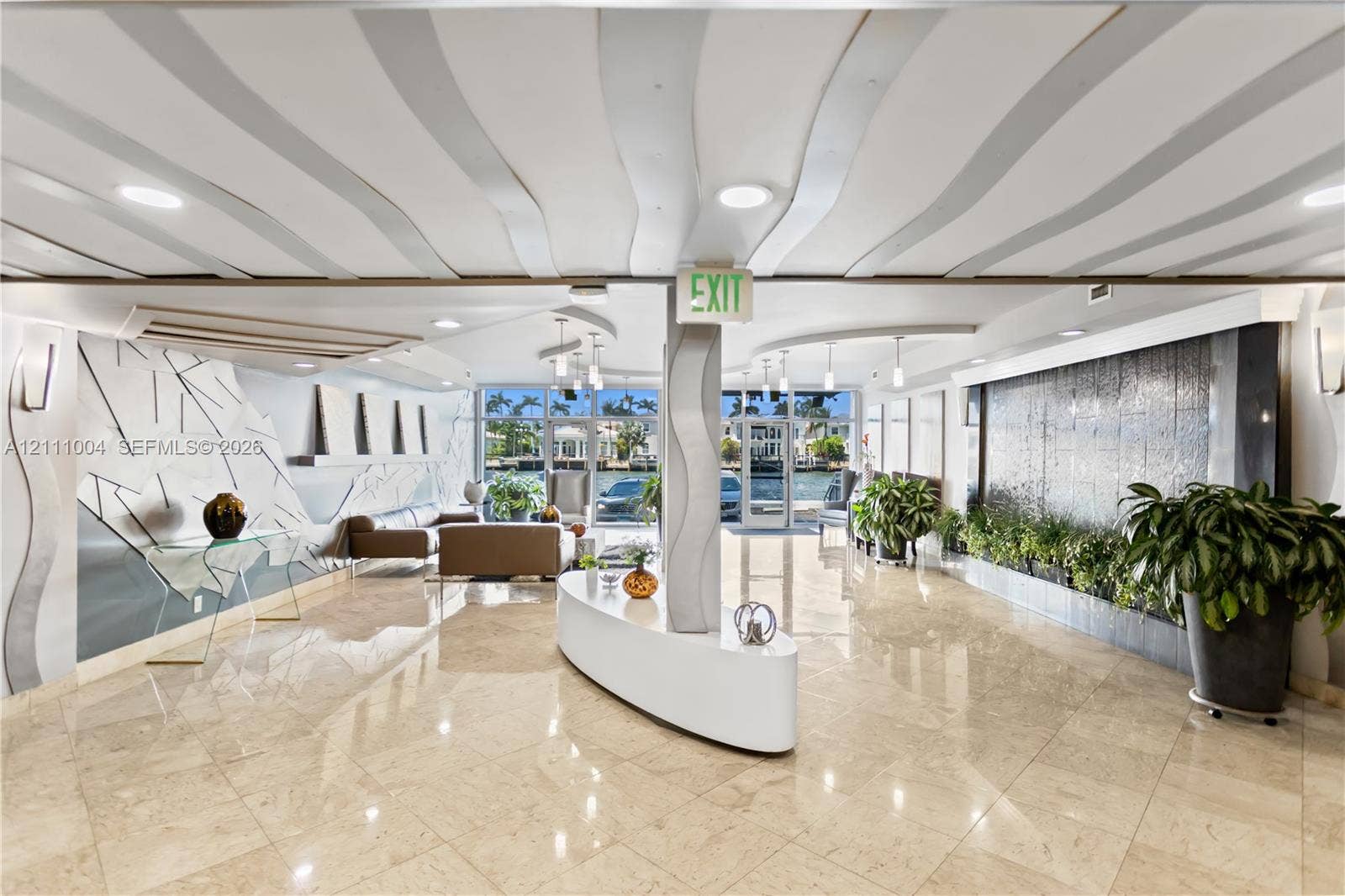 Grand lobby featuring large-format tile flooring, a custom water feature, sculptural curved ceiling detailing, recessed lighting, and a prominent geometric wall accent