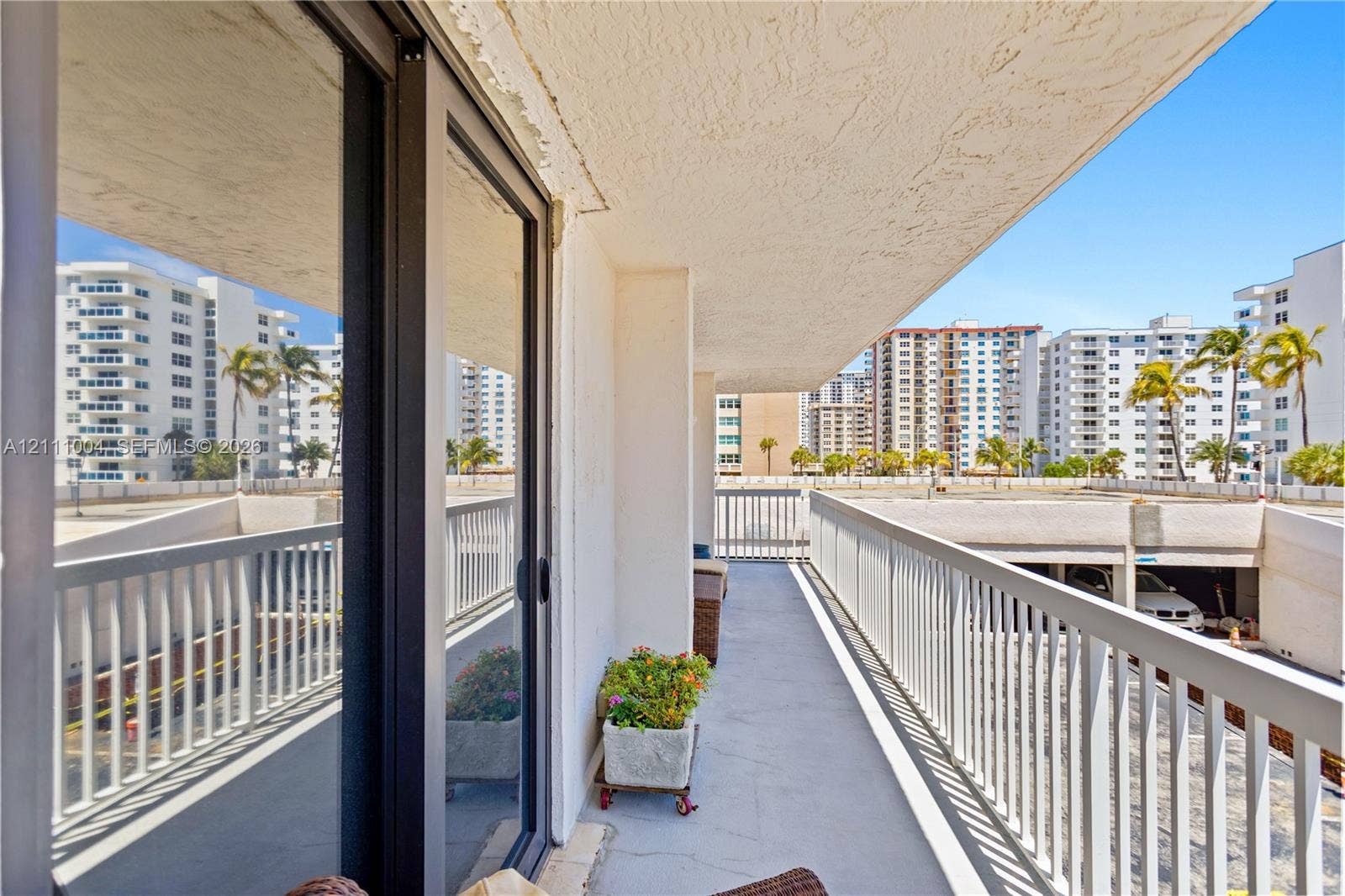 Covered balcony featuring concrete flooring, sliding glass door access, and white metal railings